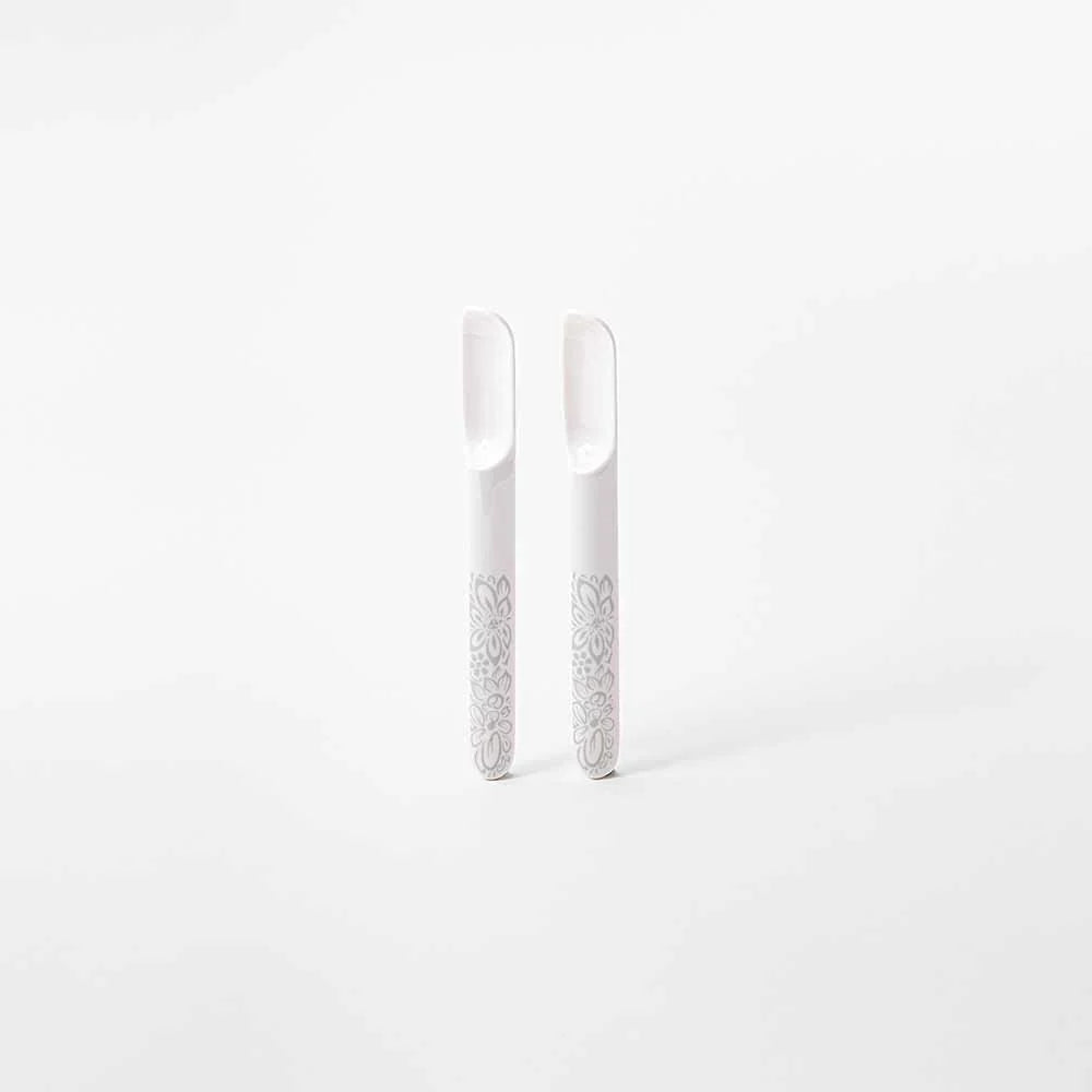 Two white ceramic nail tools with gray floral patterns on the handles, standing upright on a white background.