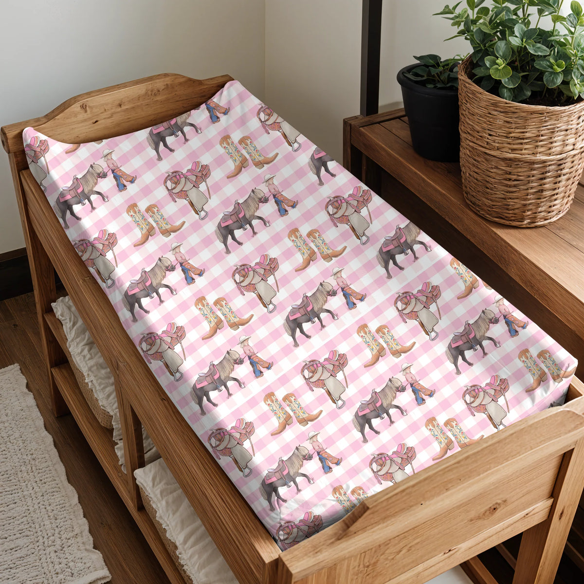 Wooden crib with pink and white checkered sheet featuring cowboy patterns.
