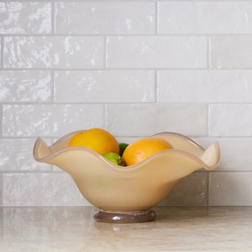 Decorative glass bowl with fruit on a kitchen counter against a tiled wall.
