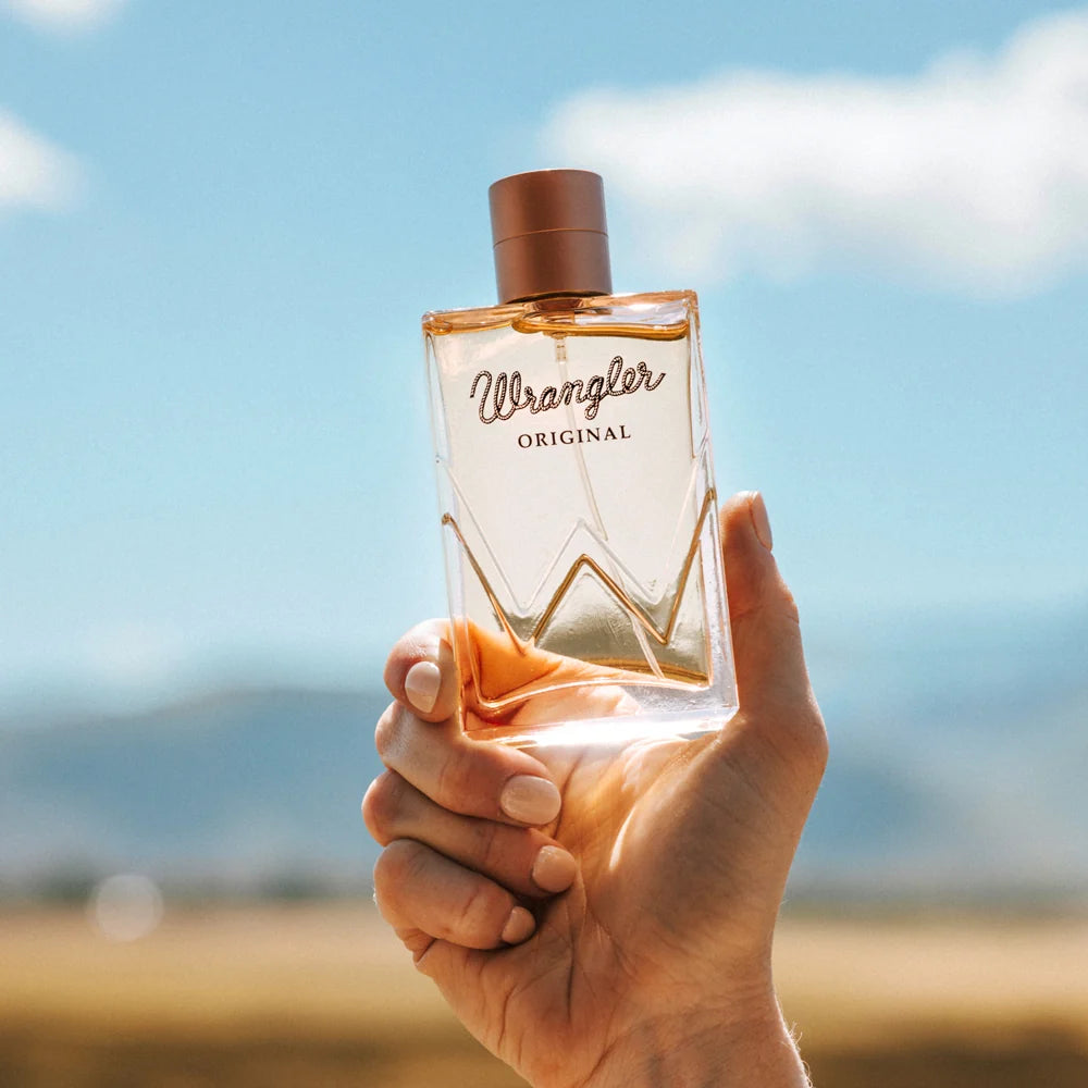 Hand holding a Wrangler Original perfume bottle against a blurred natural background