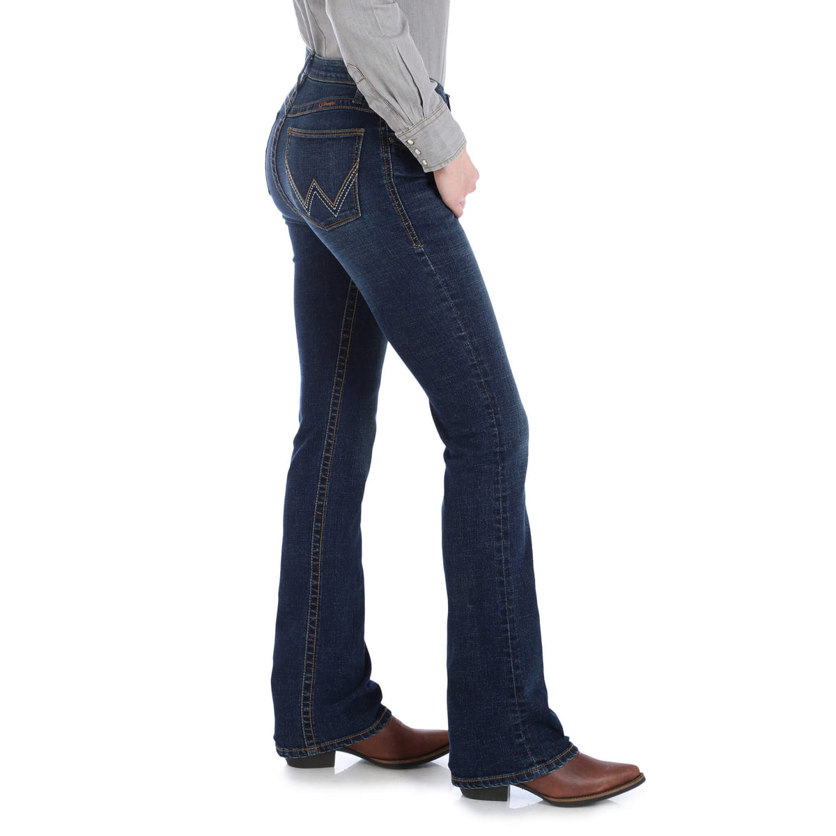 A woman standing, wearing Wrangler Women's Willow Ultimate Riding Jeans with a high-rise waist and slim fit, in a medium wash denim.