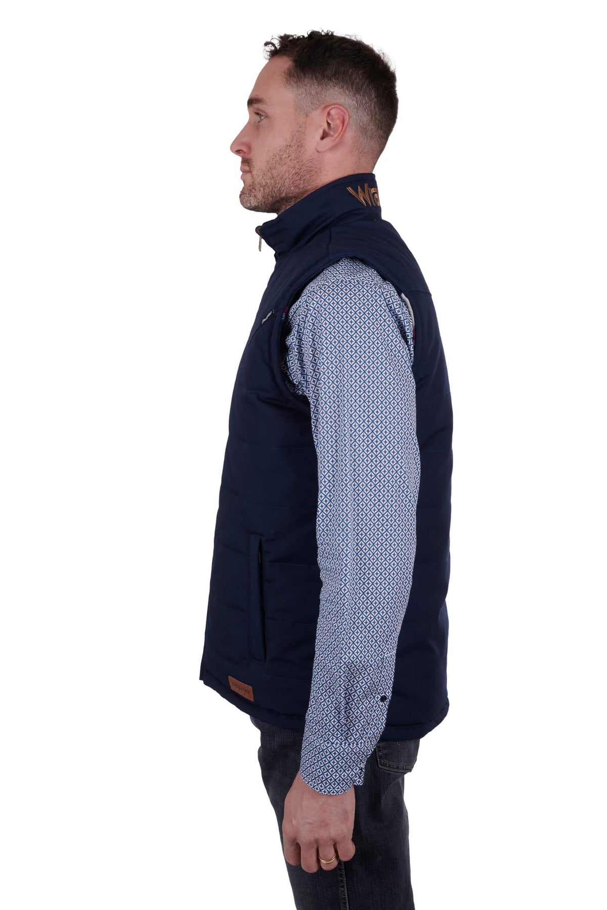 A man wearing a navy blue Wrangler reversible vest with a check pattern on the inside and a visible brand logo on the chest.
