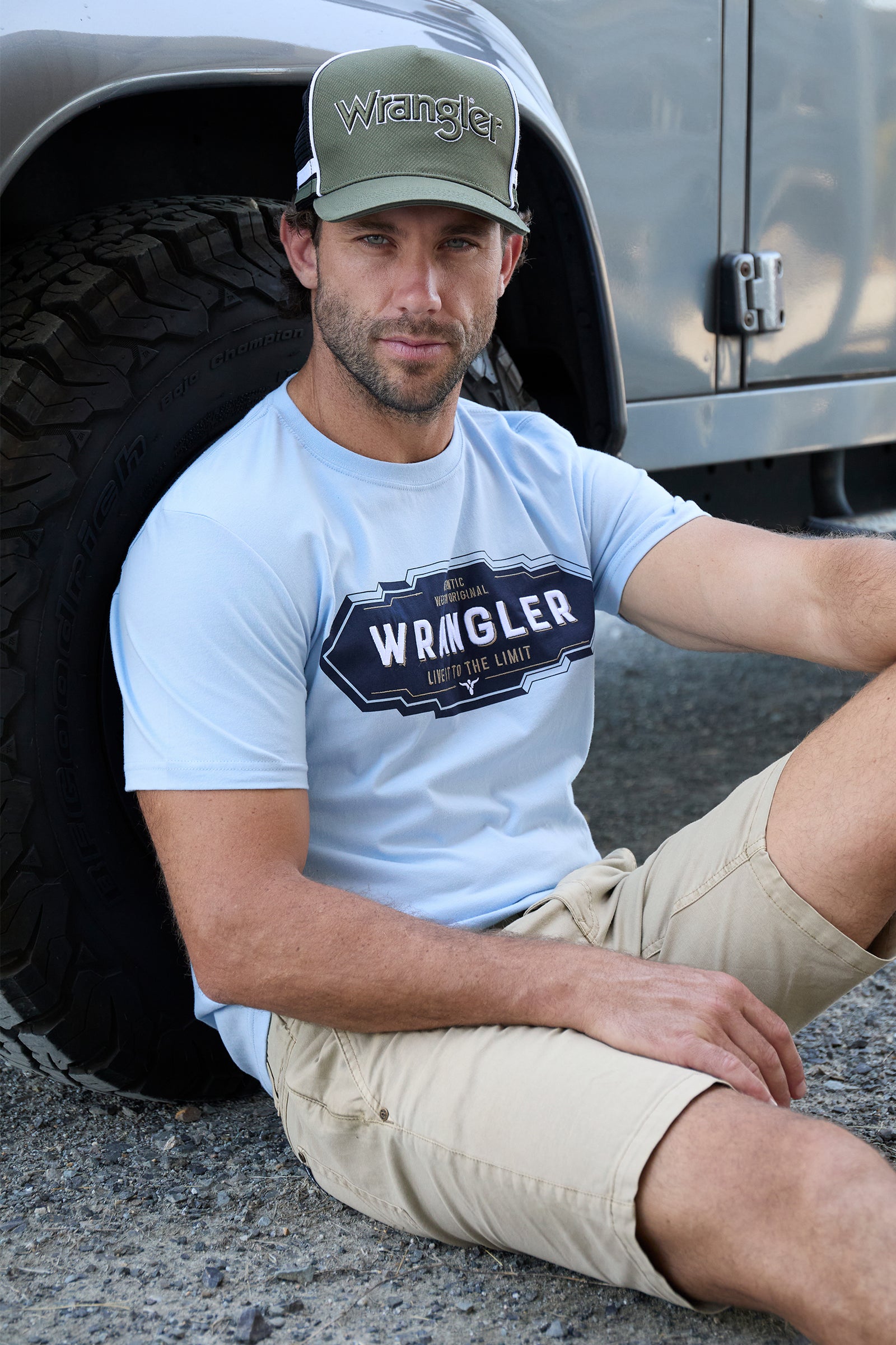 Wrangler Men's Roy S/S T-Shirt. Man wearing a Wrangler t-shirt and cap sitting next to a vehicle.