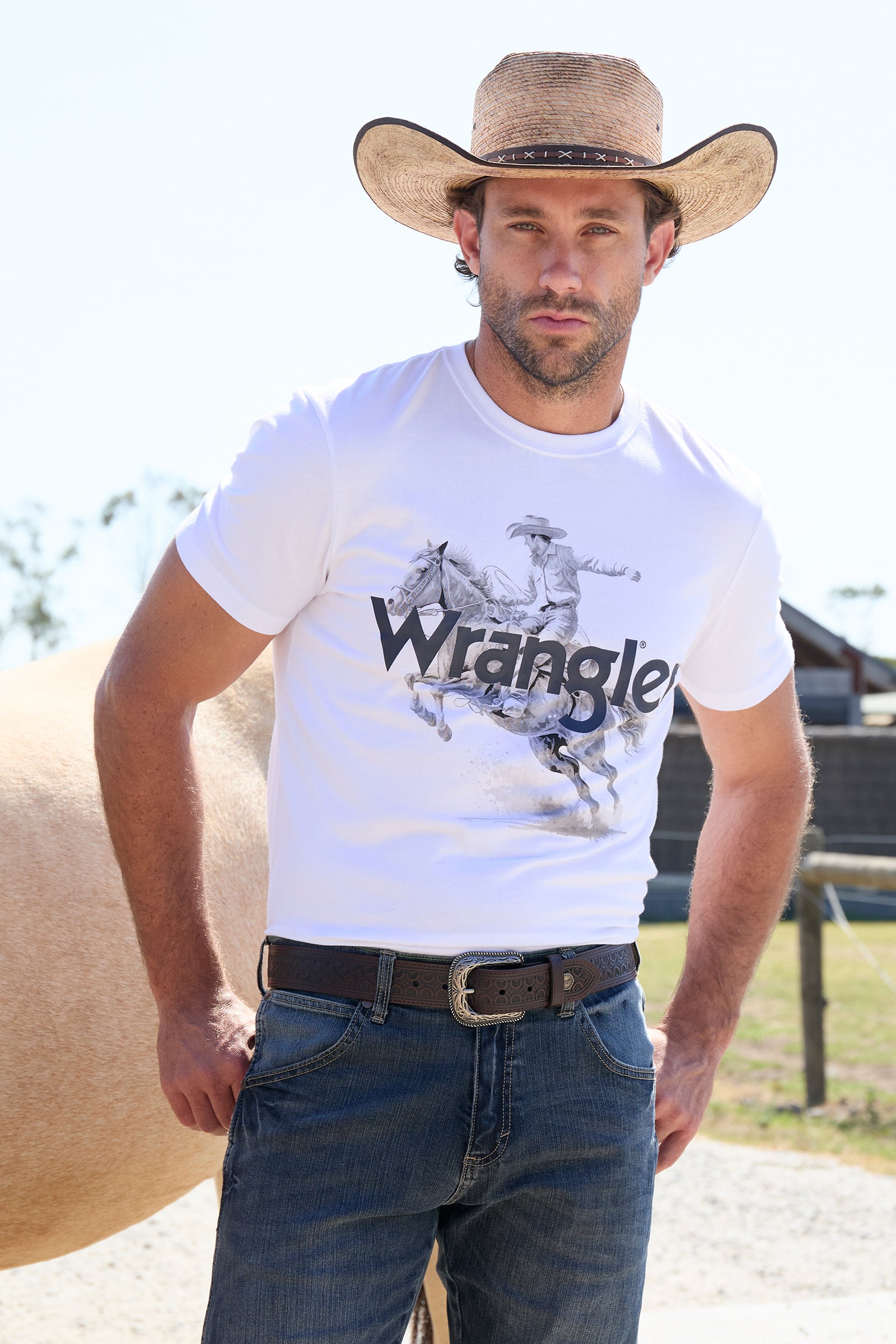 Wrangler Men's Lance S/S T-Shirt. Man wearing a white Wrangler t-shirt with a horse graphic, standing outdoors.