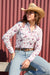 Wrangler Women's Doreen L/S Western Shirt. Woman wearing a floral shirt, jeans, and a cowboy hat against a red corrugated metal background.