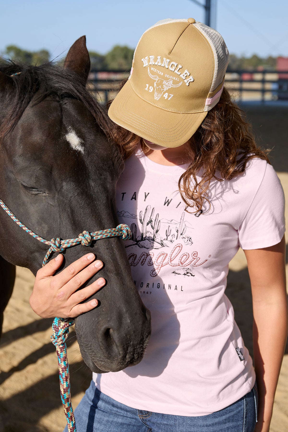 Wrangler Women's Wendy High Profile Trucker Cap. Person wearing a Wrangler cap and shirt, petting a horse in an outdoor setting