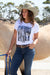Wrangler Women's Becky Western Belt. Woman wearing a white t-shirt with a graphic design, blue jeans, and a beige cowboy hat, standing next to a horse.