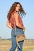 Wrangler Women's Louella Western Bag. Woman holding a beige crossbody bag with a textured design outdoors.