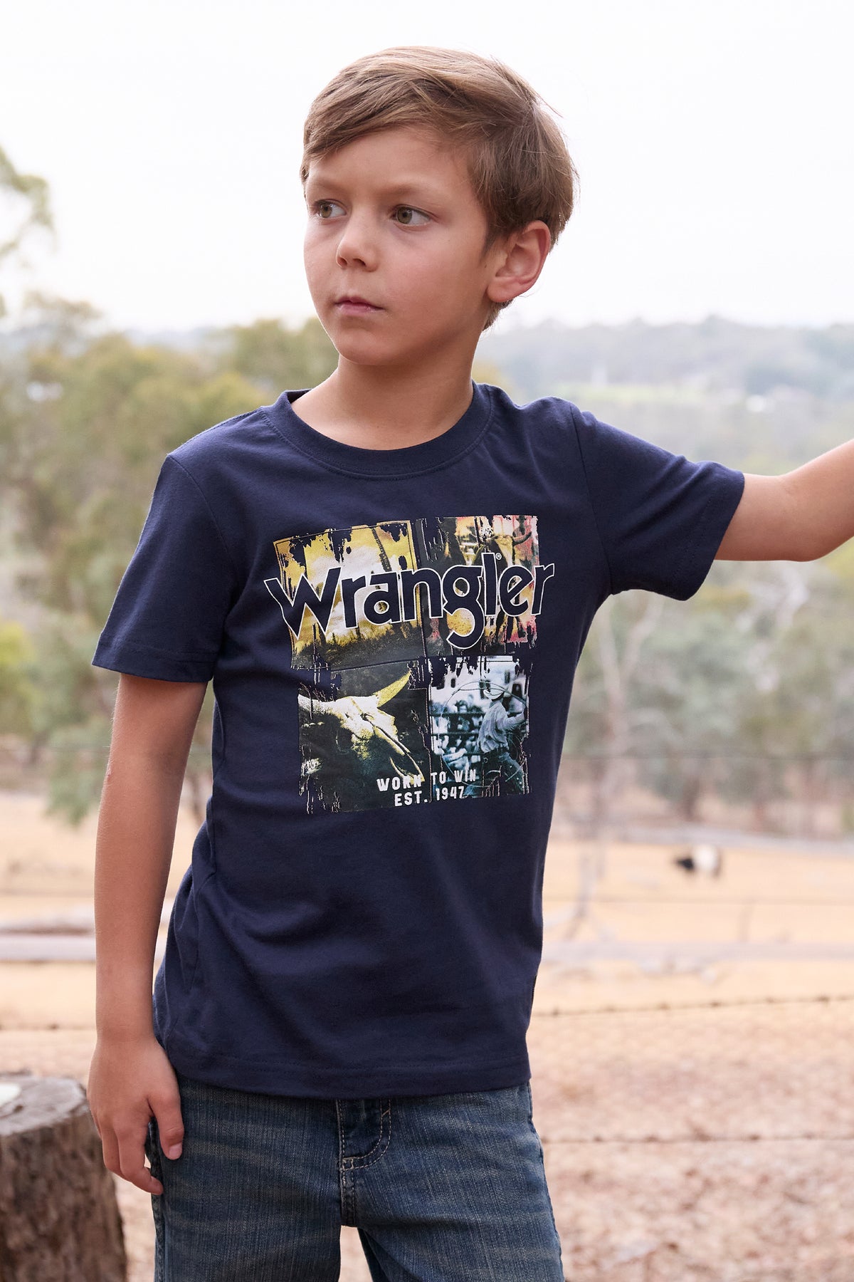 Wrangler Boy's Luis S/S T-Shirt. Child wearing a navy blue t-shirt with Wrangler logo outdoors