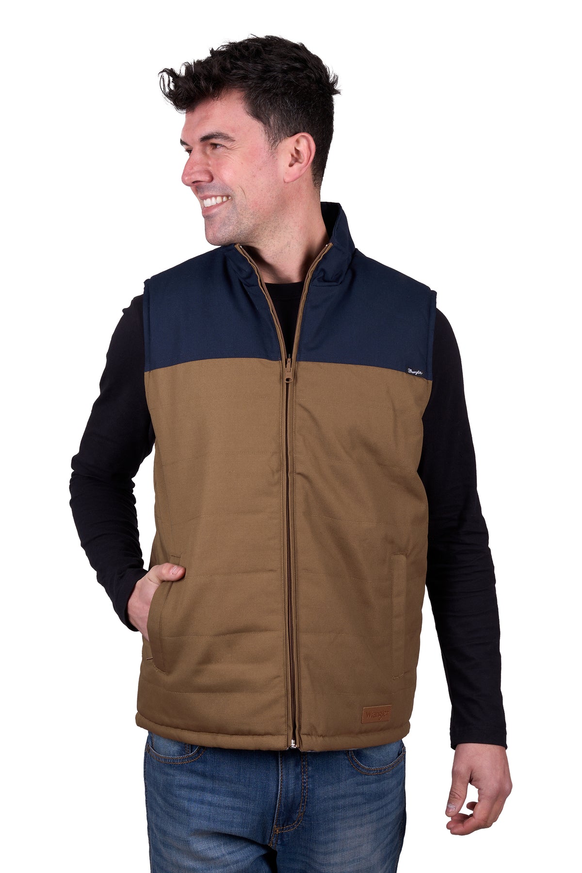 A man wearing a Wrangler Men's Koda Reversible Vest in navy and beige colors, paired with a black shirt and blue jeans.