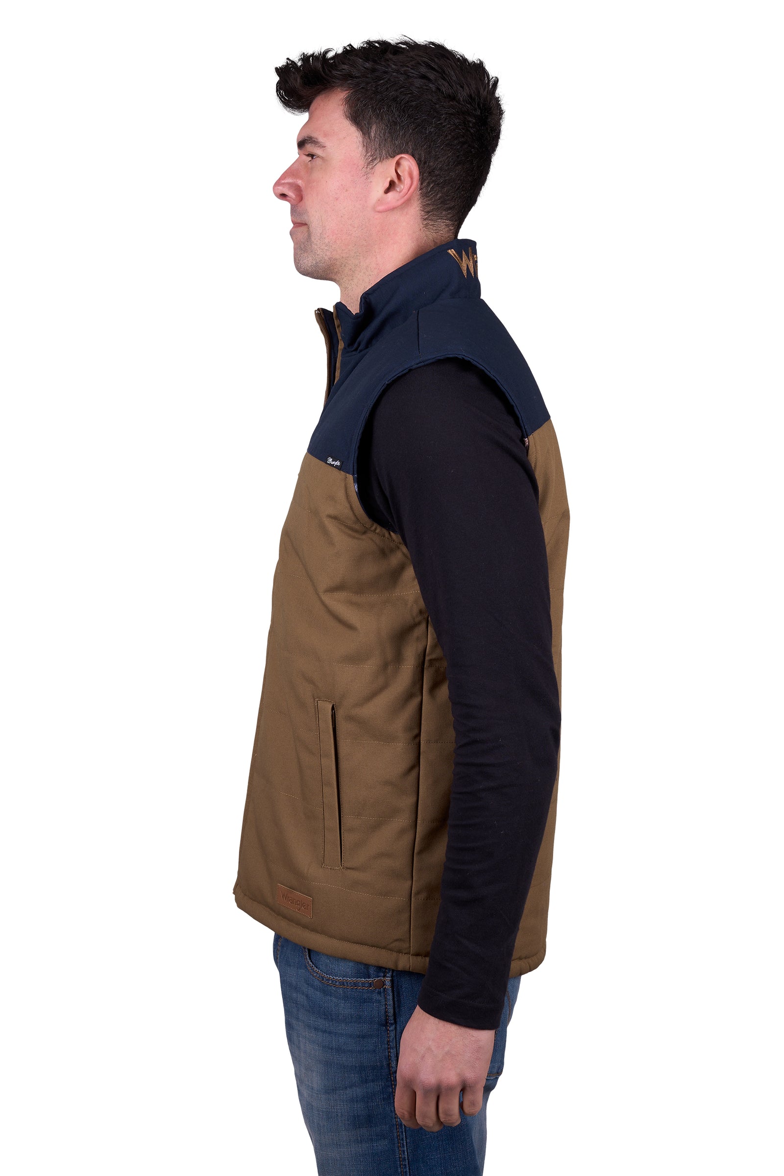 A man wearing a Wrangler Men's Koda Reversible Vest in navy and beige colors, paired with a black shirt and blue jeans.