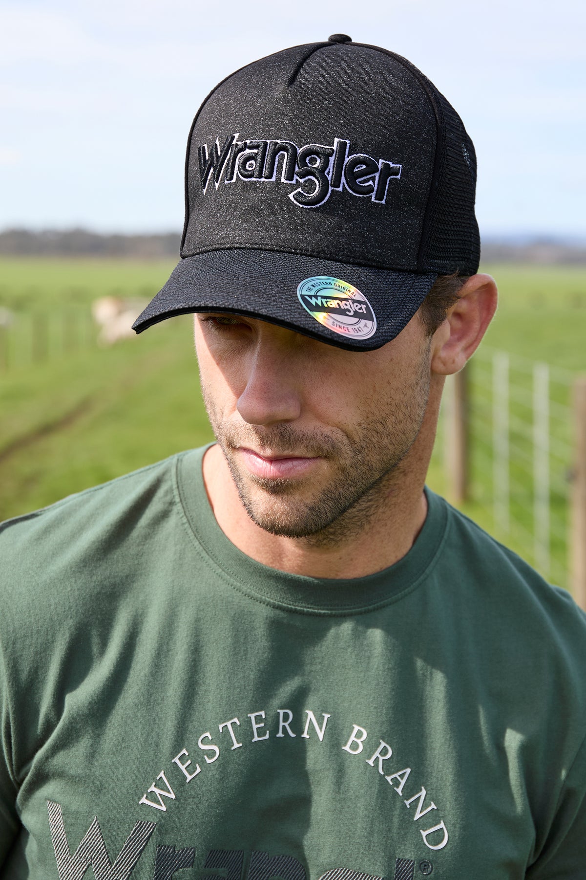 A black Wrangler branded trucker cap with a tonal printed logo, featuring a peak with mesh on the upper part and a solid color crown.