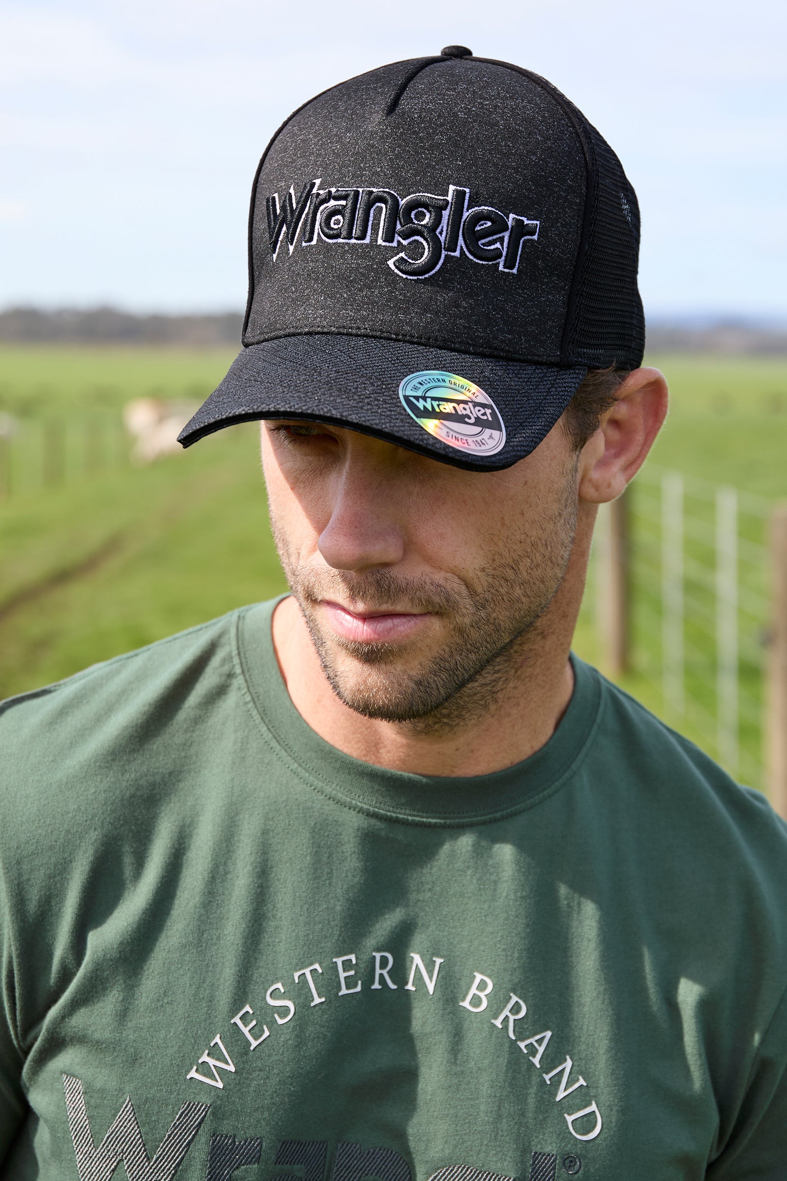A black Wrangler branded trucker cap with a tonal printed logo, featuring a peak with mesh on the upper part and a solid color crown.