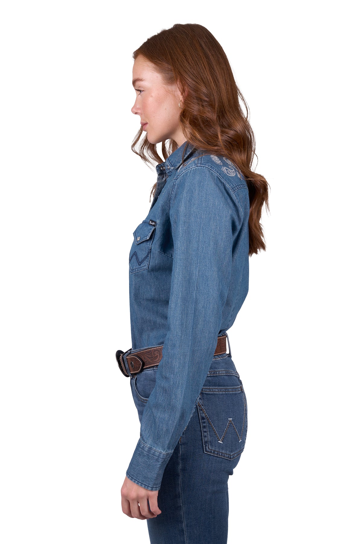 A woman wearing a wrangler western embroidered demim western shirt with paired with blue jeans.