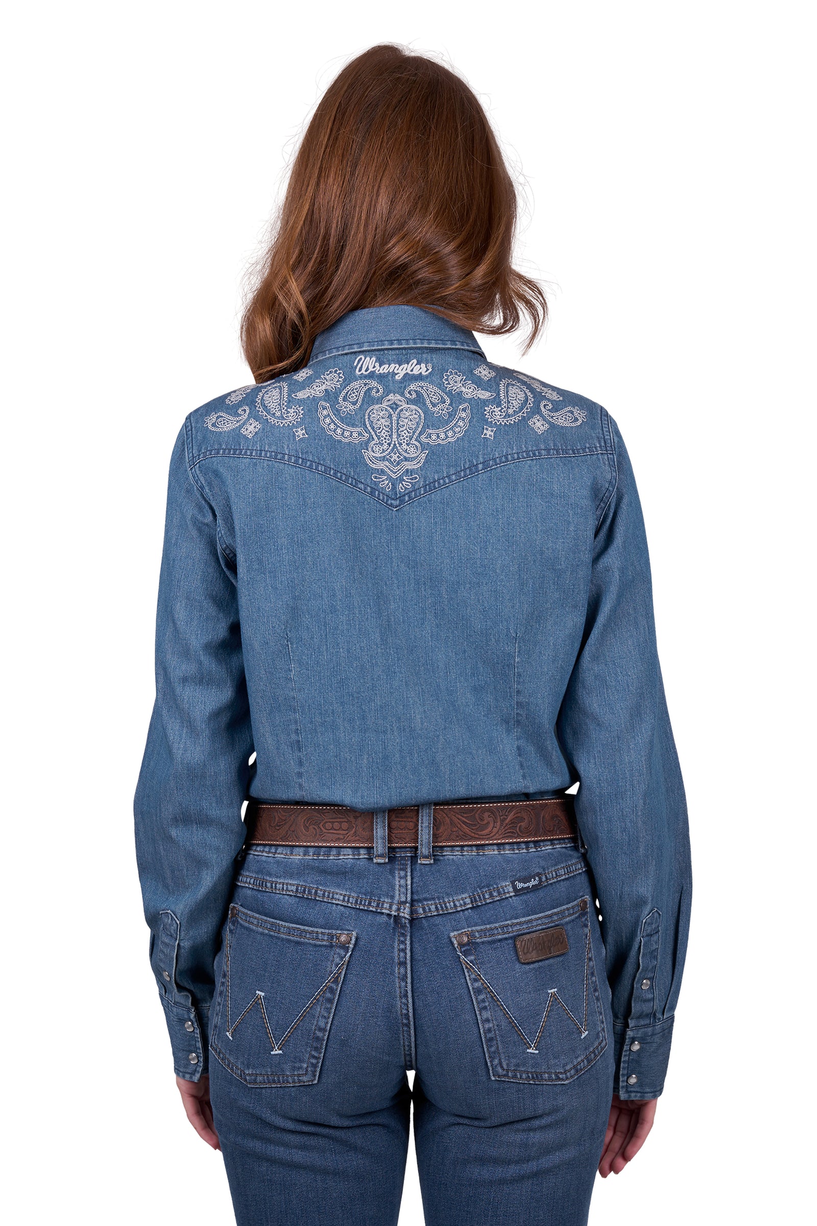 A woman wearing a wrangler western embroidered demim western shirt with paired with blue jeans.