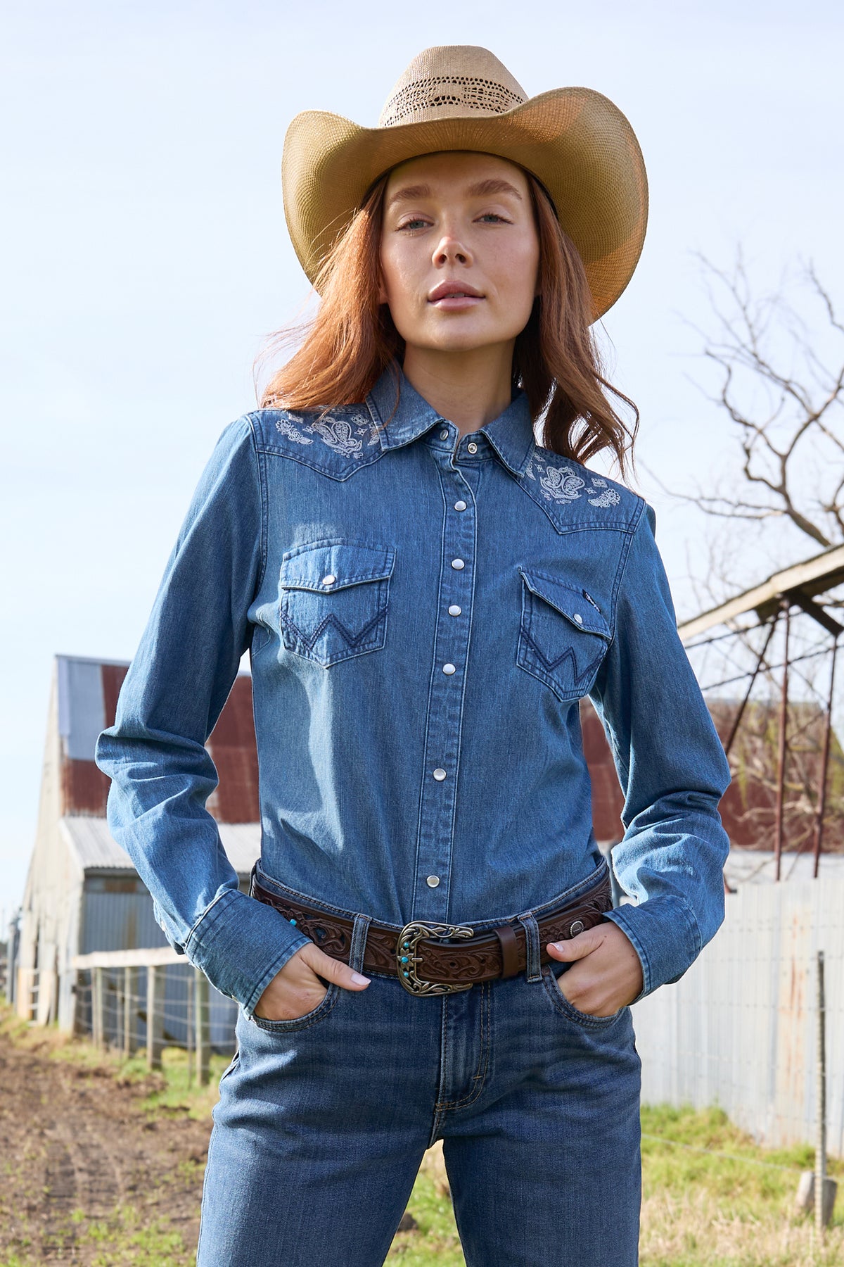 A woman wearing a wrangler western embroidered demim western shirt with paired with blue jeans.