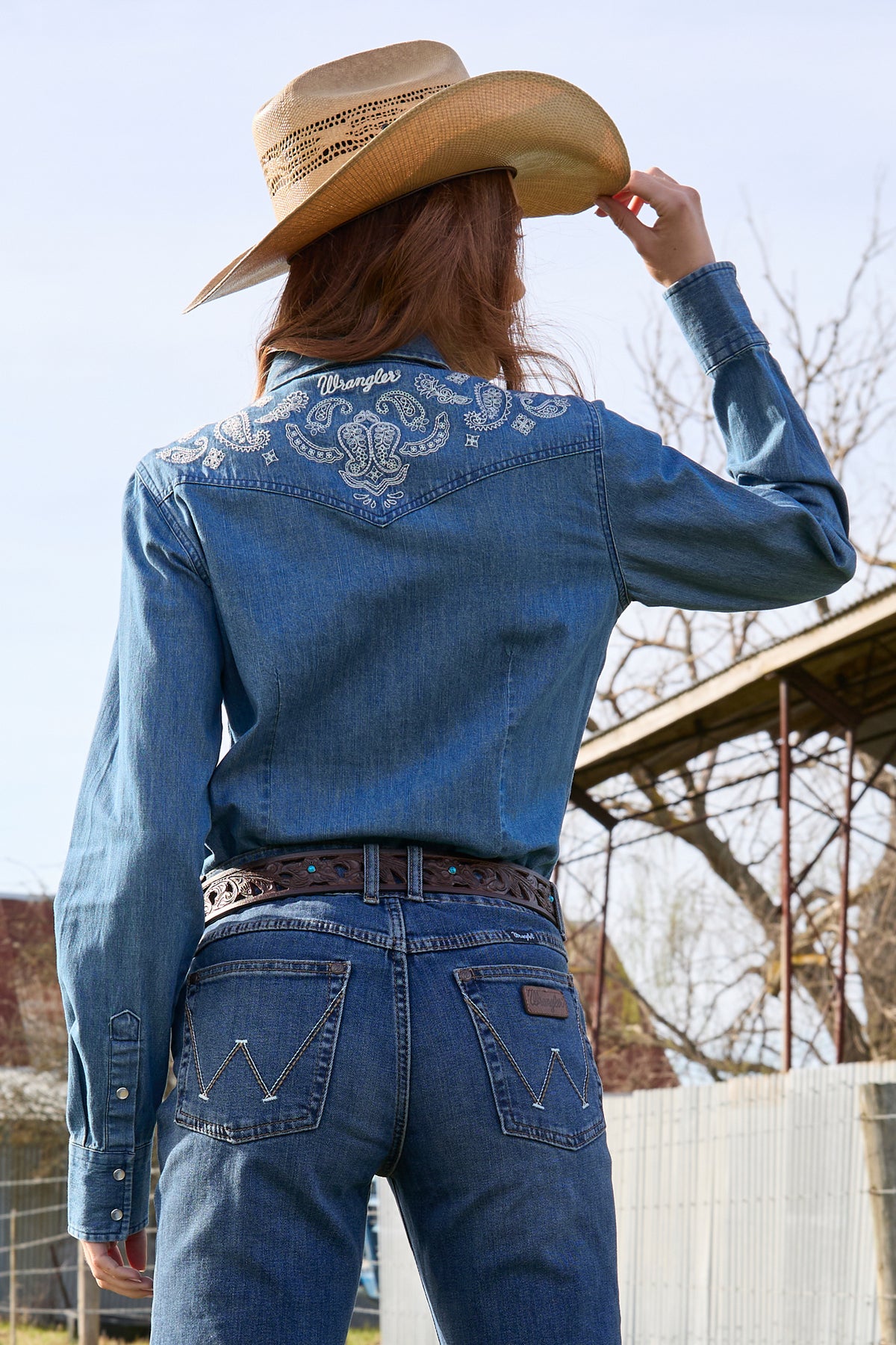 A woman wearing a wrangler western embroidered demim western shirt with paired with blue jeans.