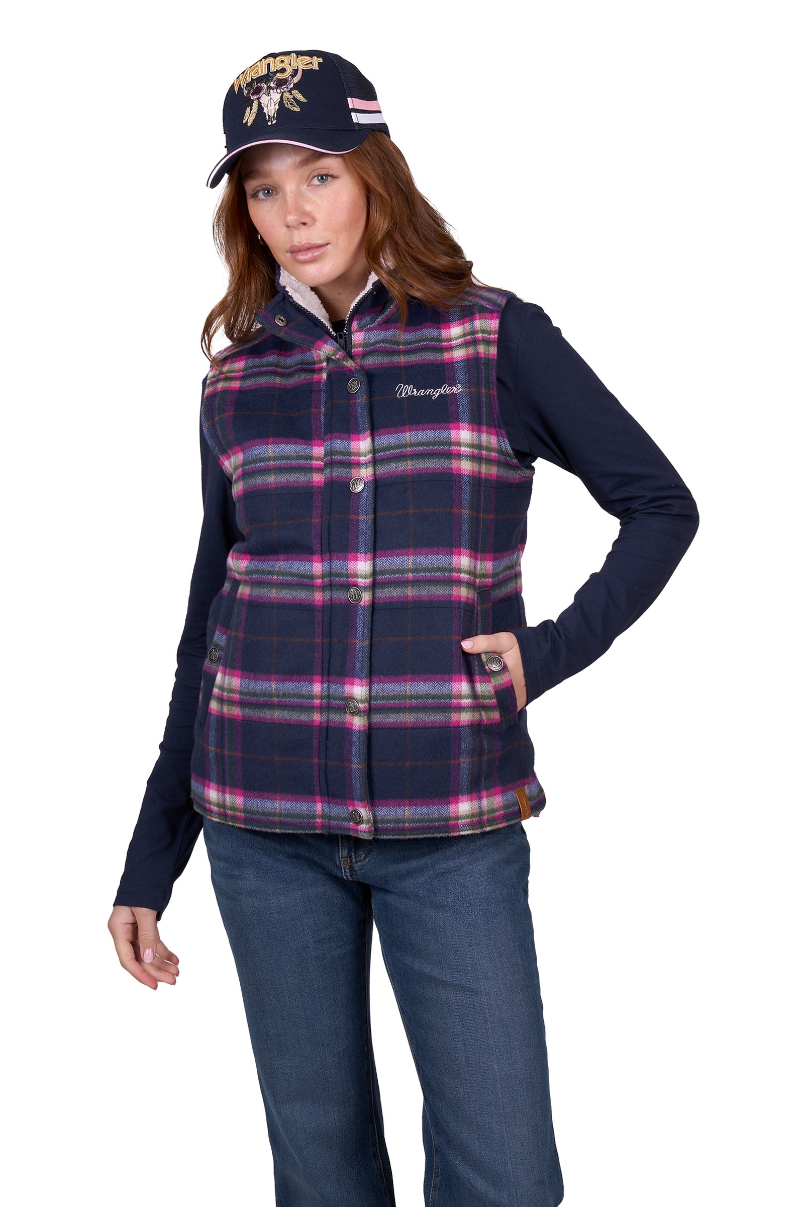 A woman wearing a purple and pink plaid vest with a sherpa collar, over a blue shirt, paired with jeans.