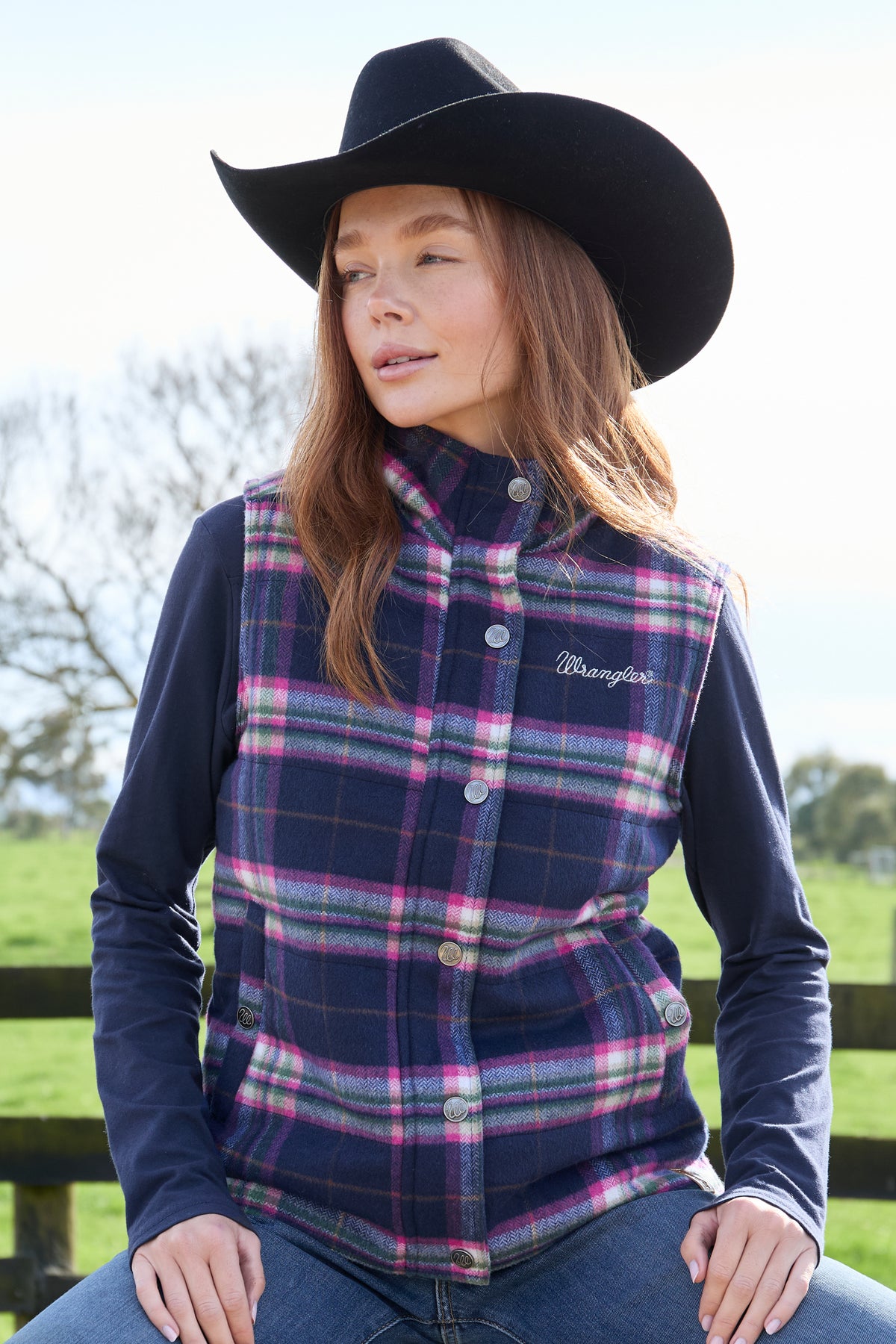 A woman wearing a purple and pink plaid vest with a sherpa collar, over a blue shirt, paired with jeans.