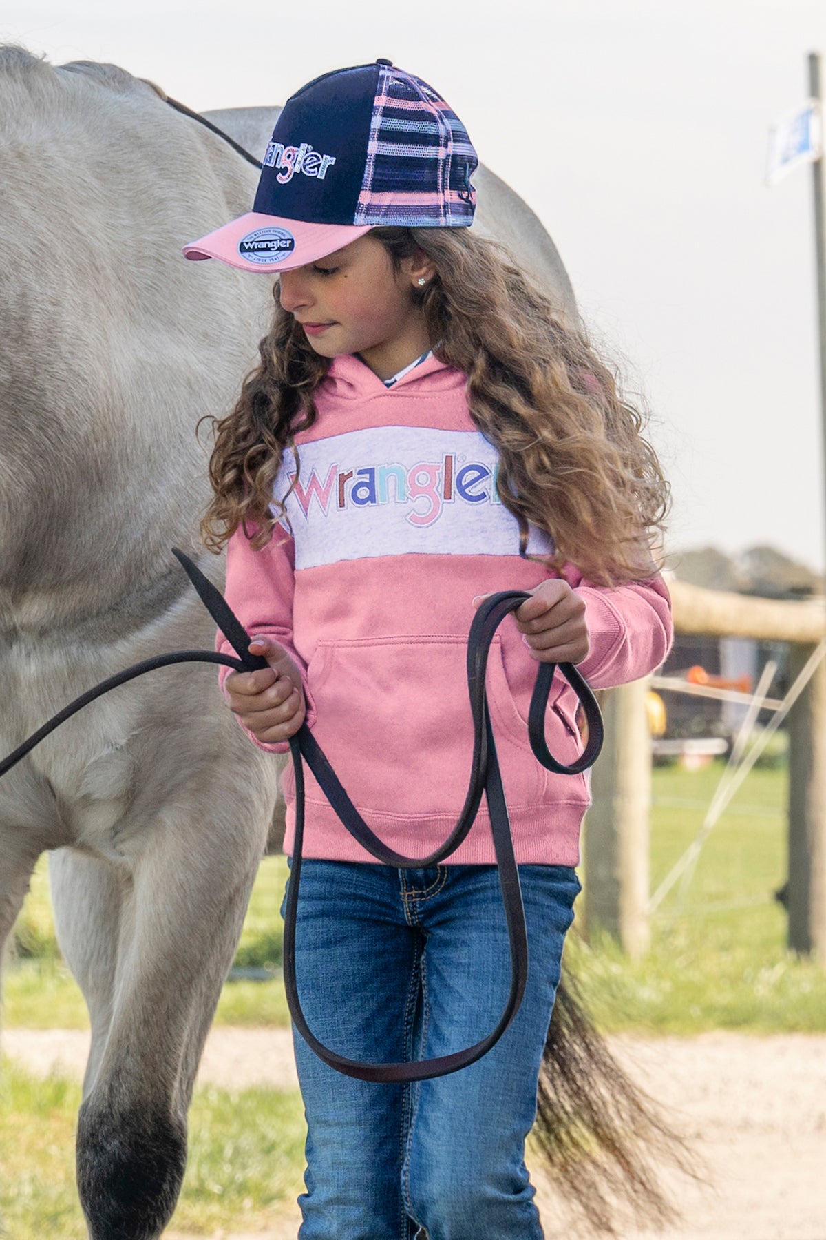 A girl's high pony tail cap with a cutout, featuring a multicolor design with a pink brim and a 'Wrangler' logo on the front.