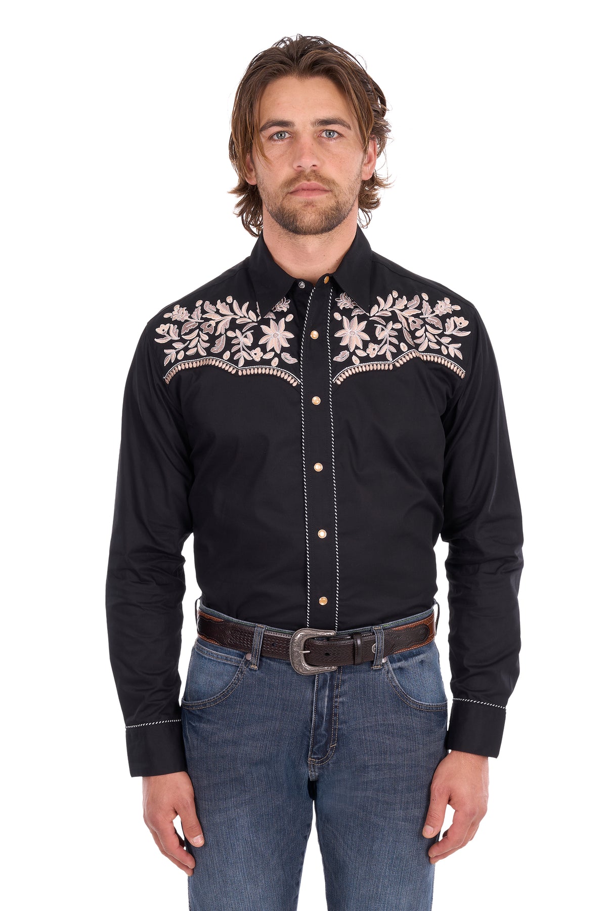 A man wearing a black long-sleeve western-style button-down shirt with white floral embroidery across the chest, paired with blue jeans and a brown belt, photographed against a plain white background.