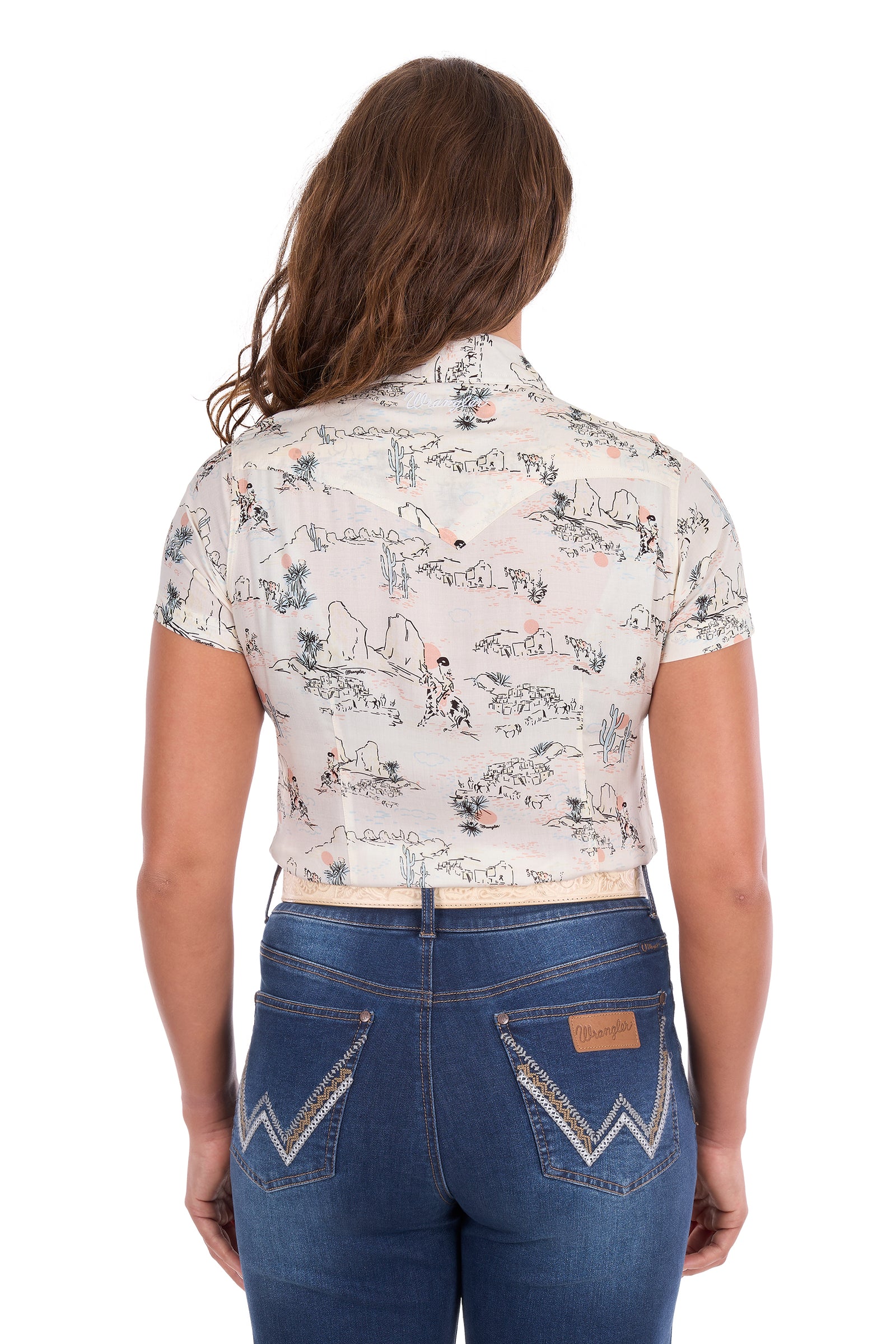 A woman viewed from the back wearing a short-sleeve cropped western shirt with a beige and blue scenic print, paired with blue jeans.