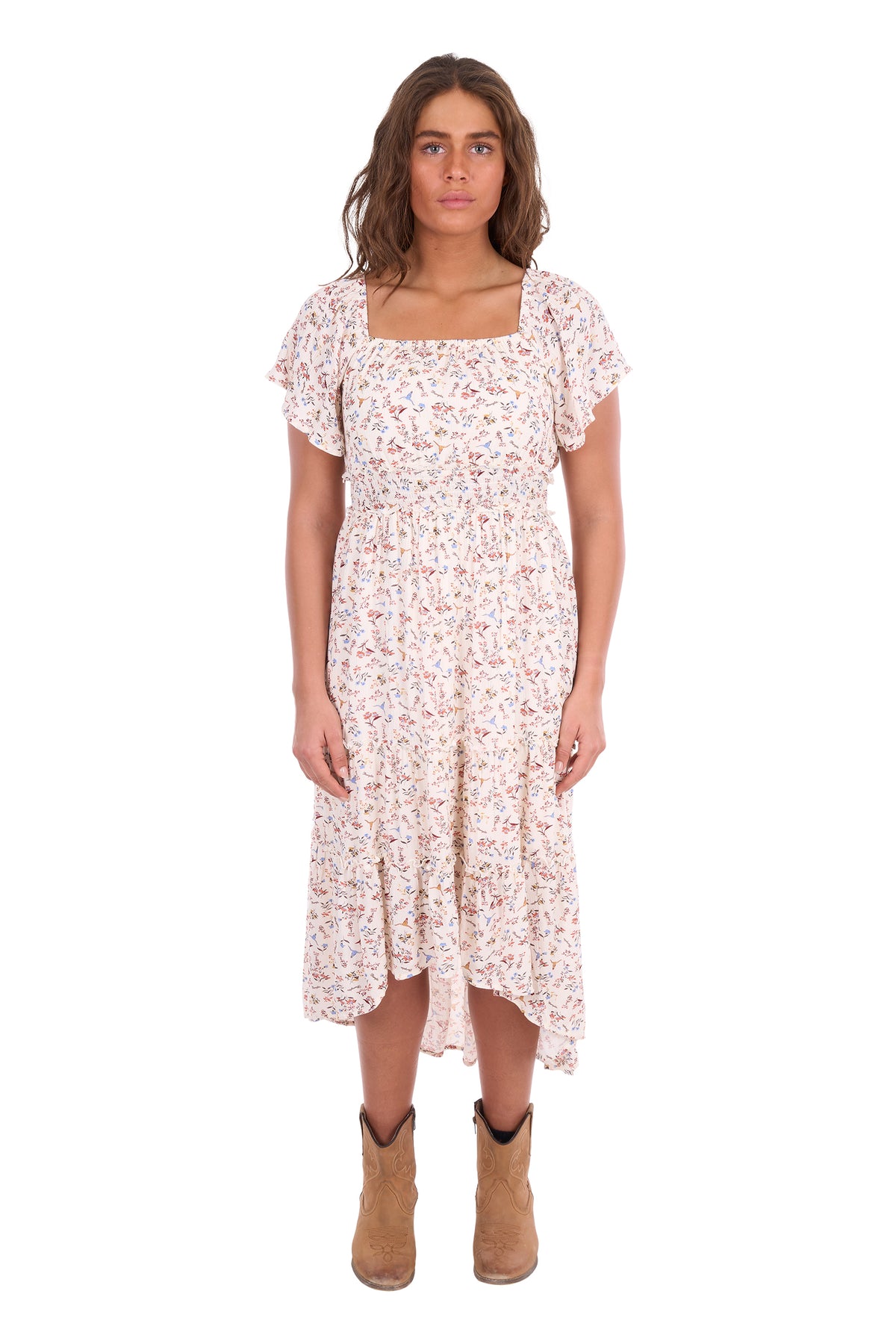 A woman modeling a short-sleeve midi dress with a delicate pink and green floral print on a cream background, paired with tan ankle boots, against a plain white studio background.