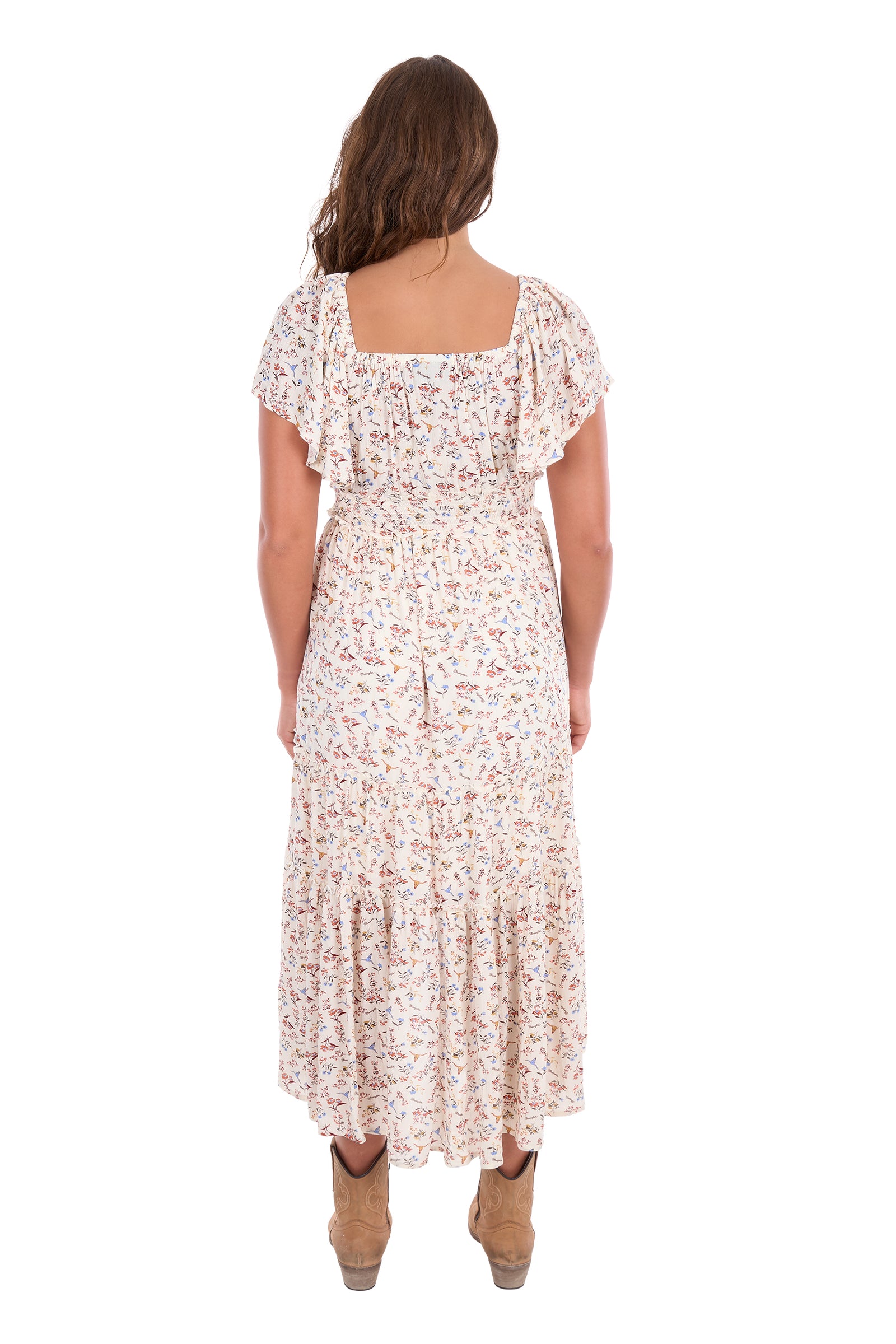 A woman viewed from the back wearing a long floral midi dress with flutter sleeves and a square neckline, paired with tan ankle boots, against a plain white background.
