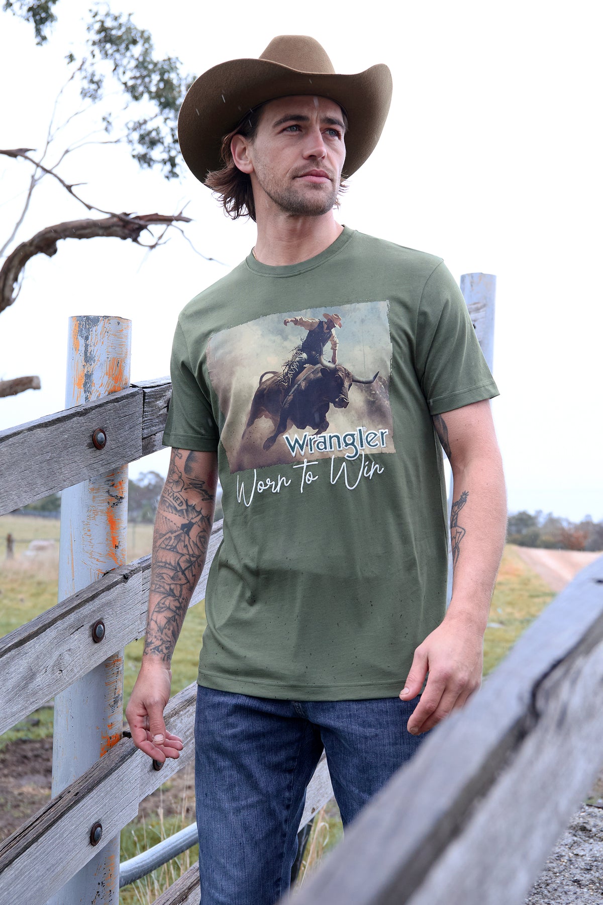 Man wearing a green t-shirt with a graphic design, standing outdoors near a wooden fence.