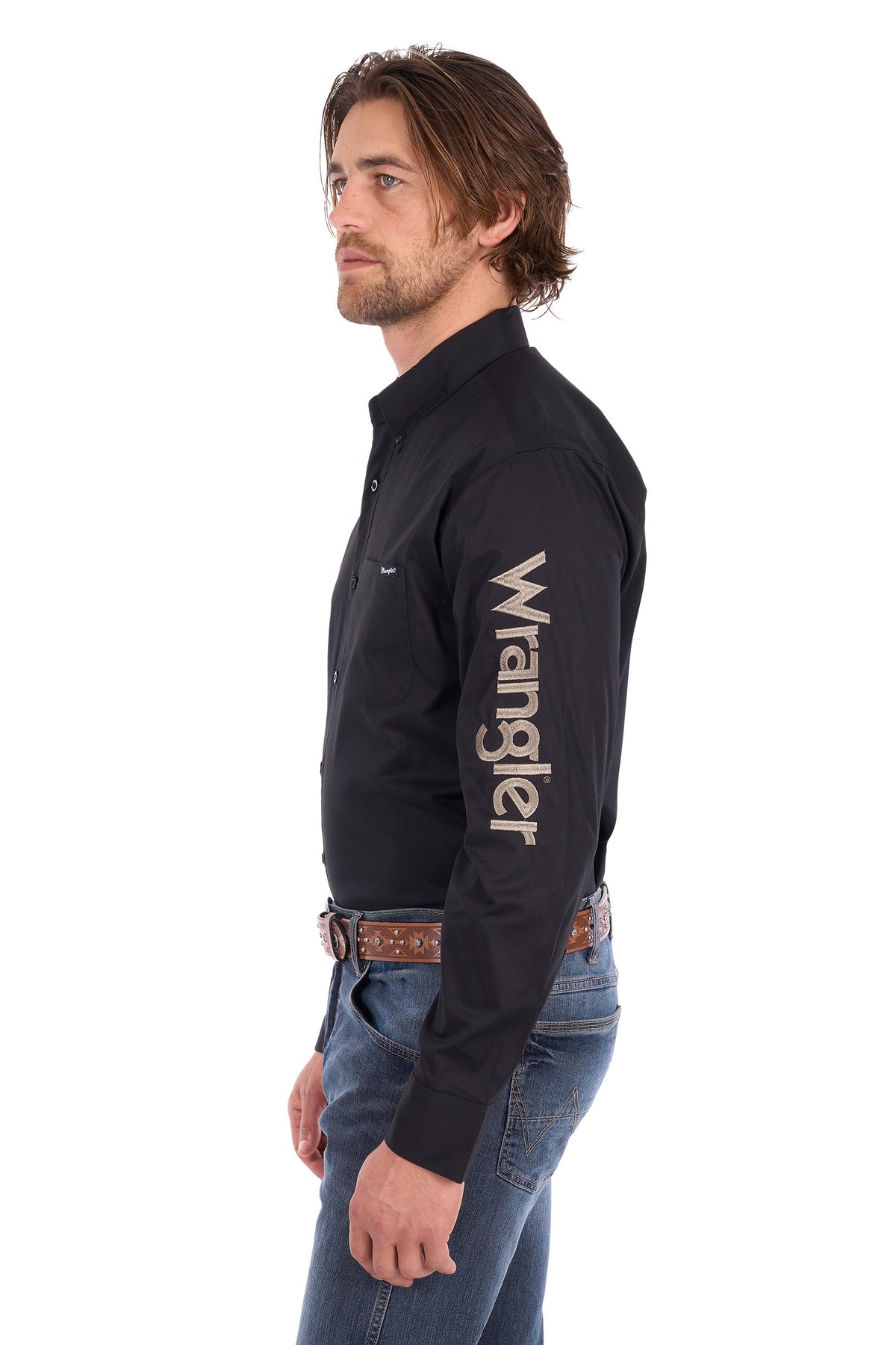 A man shown in profile wearing a black long-sleeve Wrangler button-up shirt with a large white logo printed vertically down the right sleeve, paired with blue jeans and a brown patterned belt, against a plain white background.