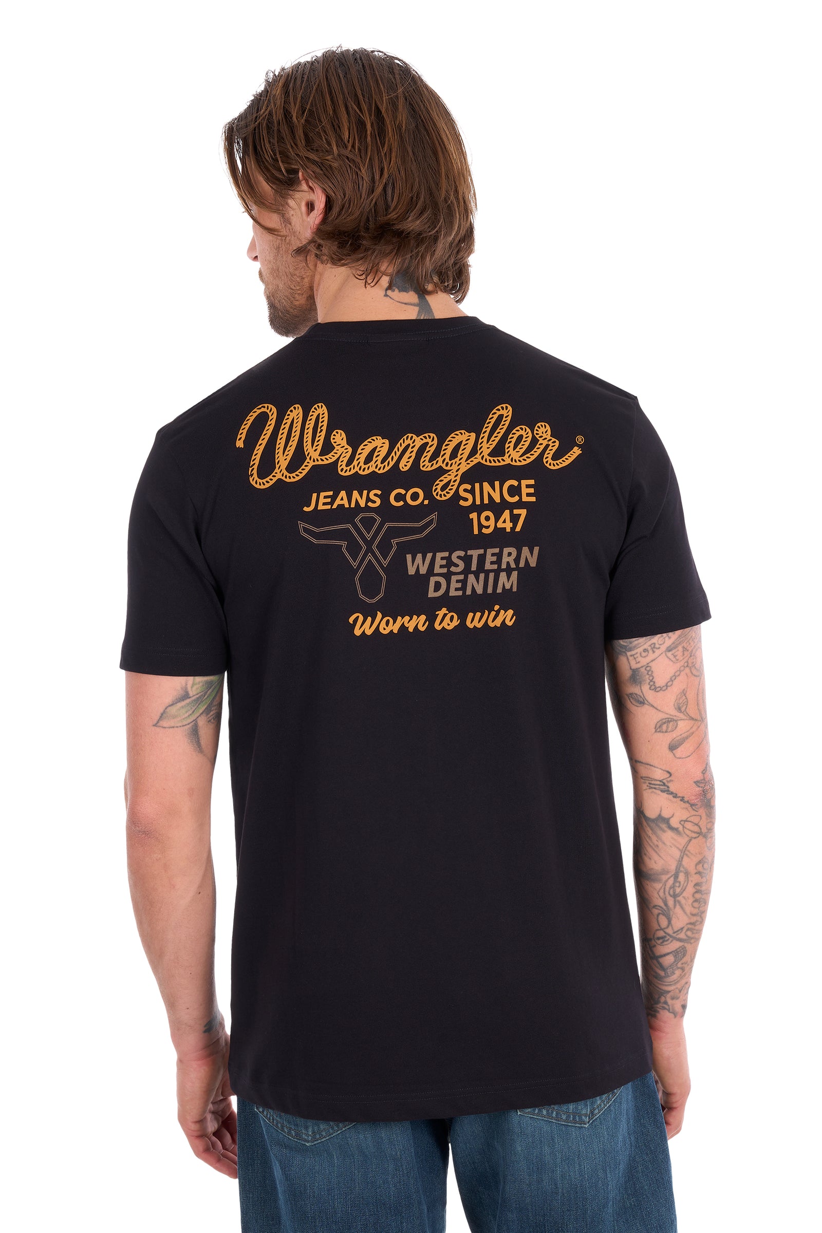 A man viewed from the back wearing a black Wrangler t-shirt with a large gold and white graphic print on the back, paired with blue jeans against a white background.