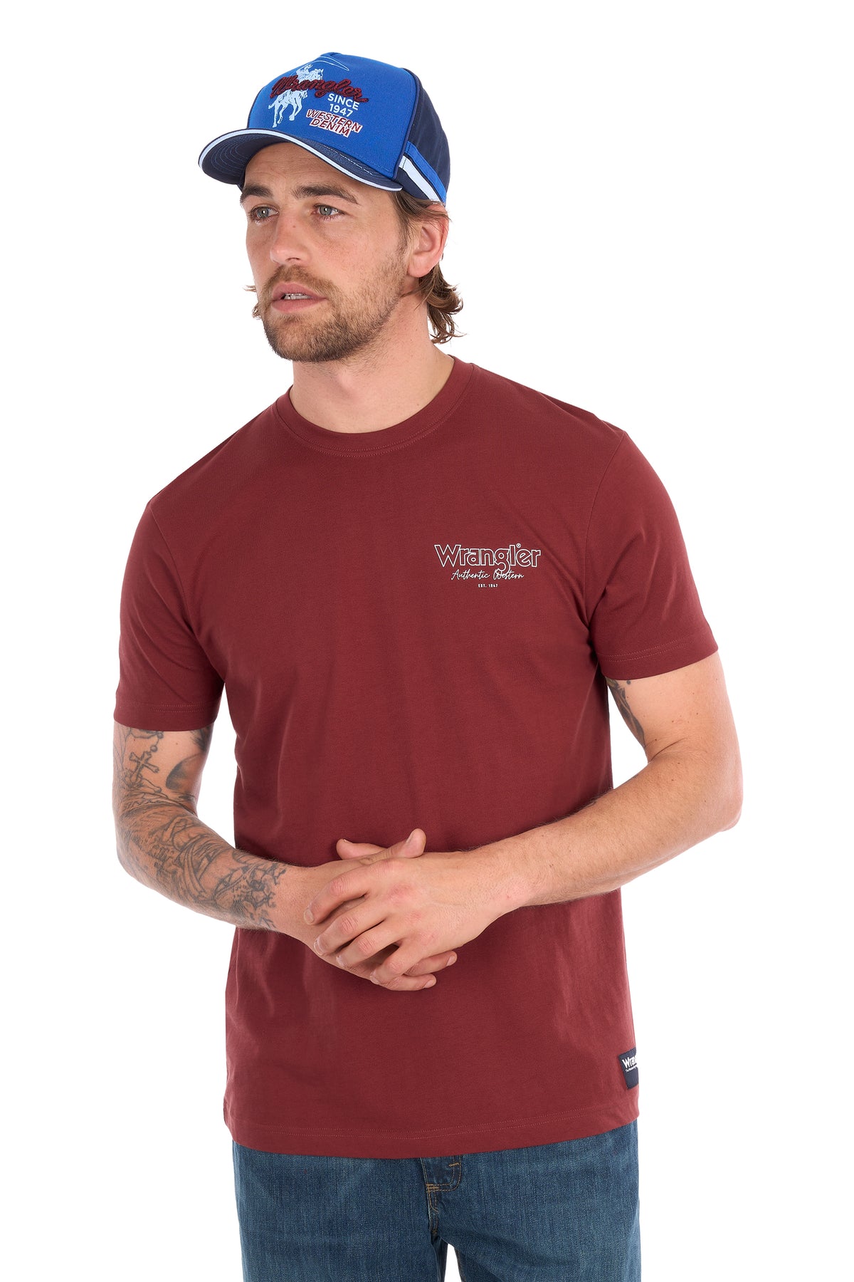 A man wearing a maroon Wrangler short-sleeve t-shirt and a blue trucker hat, standing against a white background.