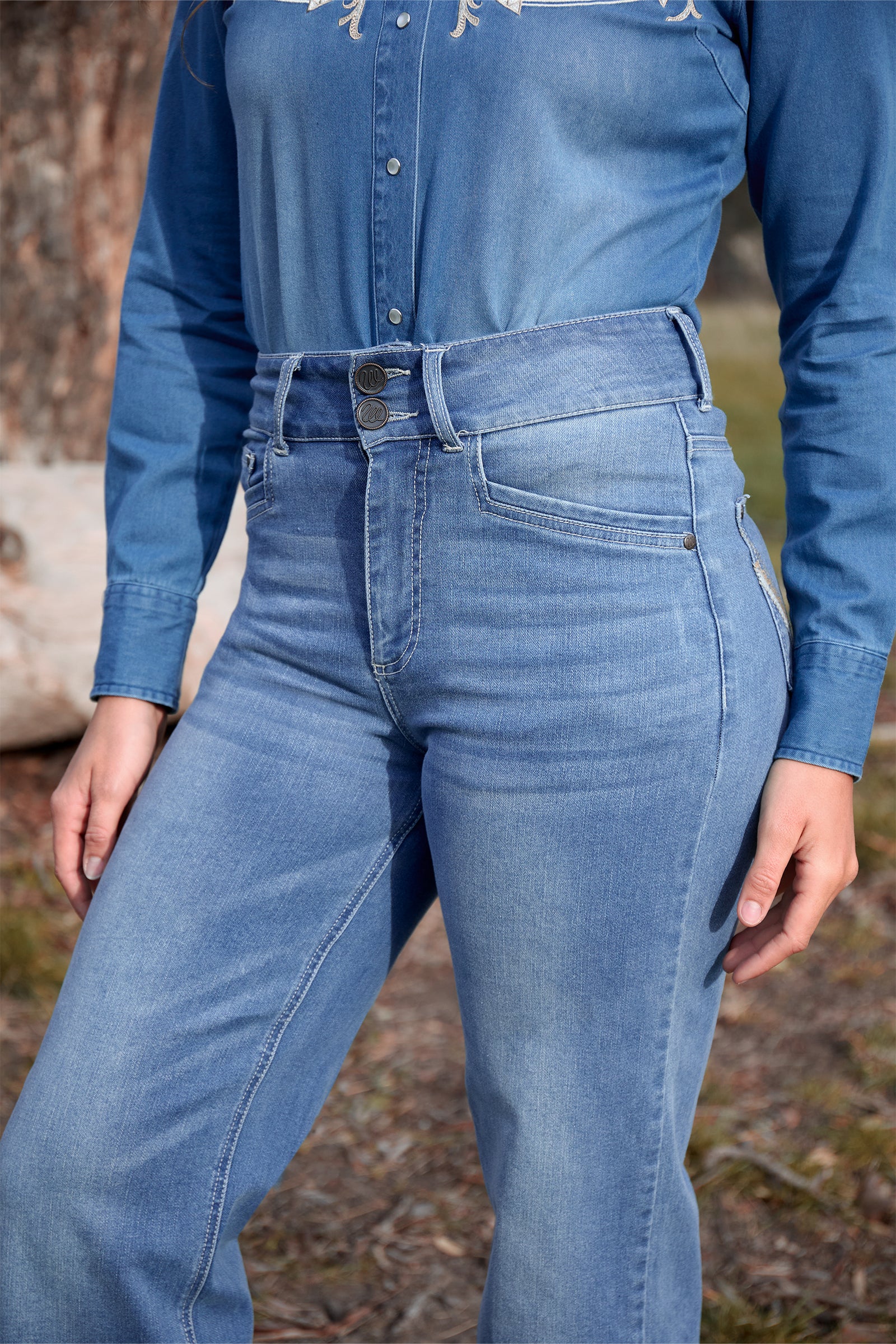 Person wearing a blue denim shirt and jeans outdoors.