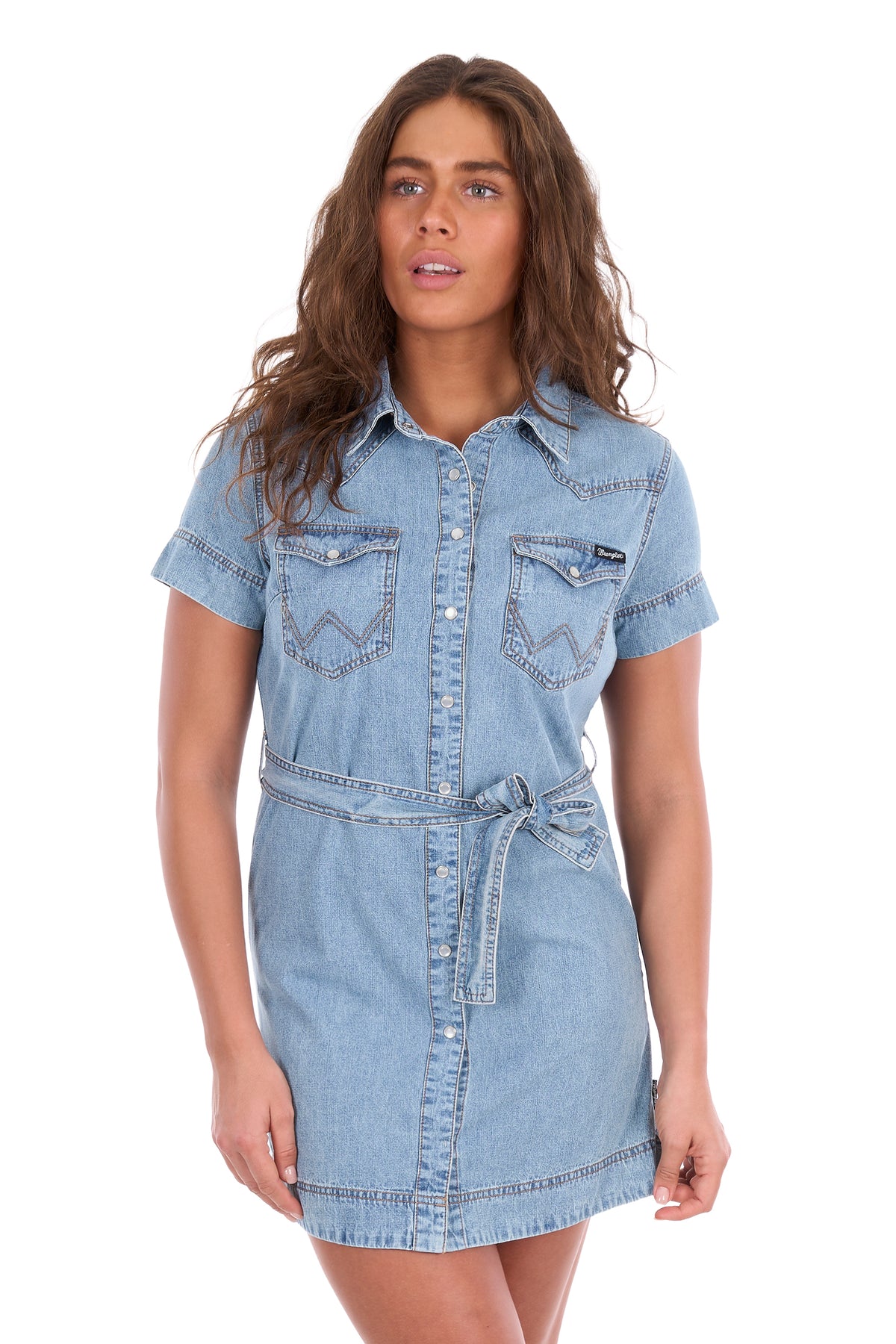 A woman modeling a light blue denim shirt dress with short sleeves, a button-up front, chest flap pockets, and a matching denim tie belt at the waist, photographed against a plain white background.