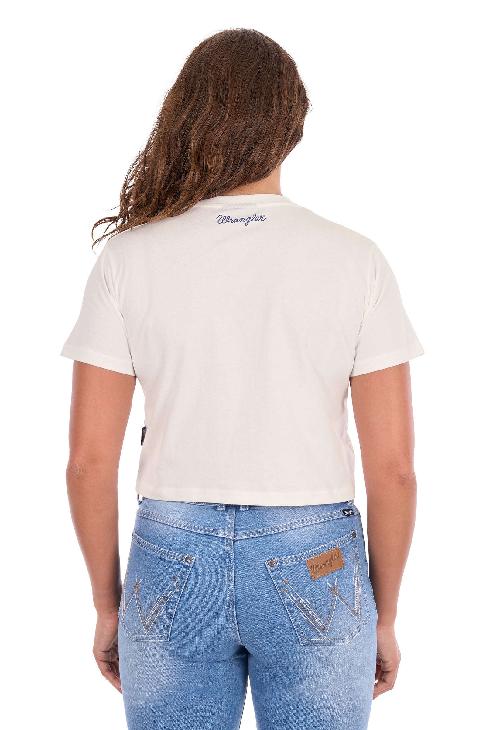 A woman viewed from the back wearing a short-sleeve cream-colored Wrangler t-shirt and light blue denim jeans against a white background.