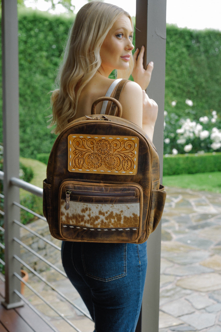 Woman wearing a brown leather backpack with decorative elements outdoors.