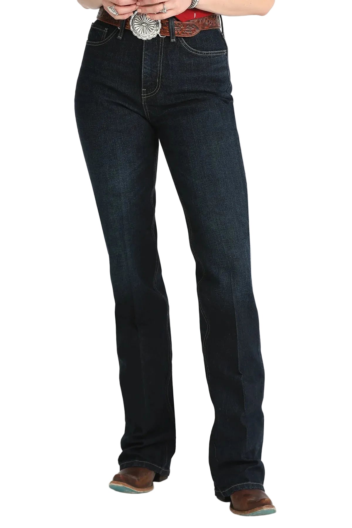 A person wearing dark blue straight-leg denim jeans with a brown leather belt and a large silver concho buckle, paired with brown boots, against a white studio background.