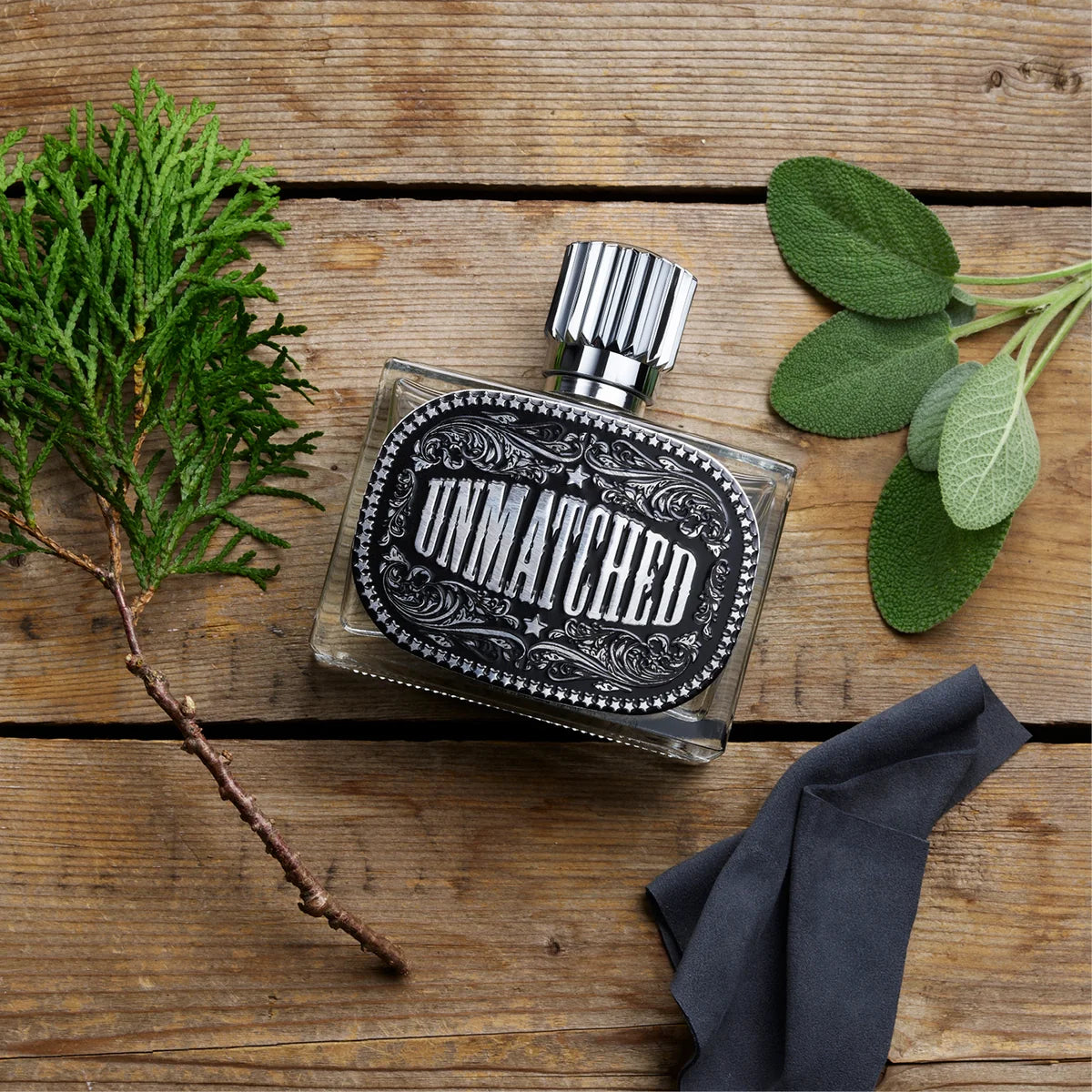 Perfume bottle labeled 'Unmatched' on a wooden surface with green leaves and a dark cloth.