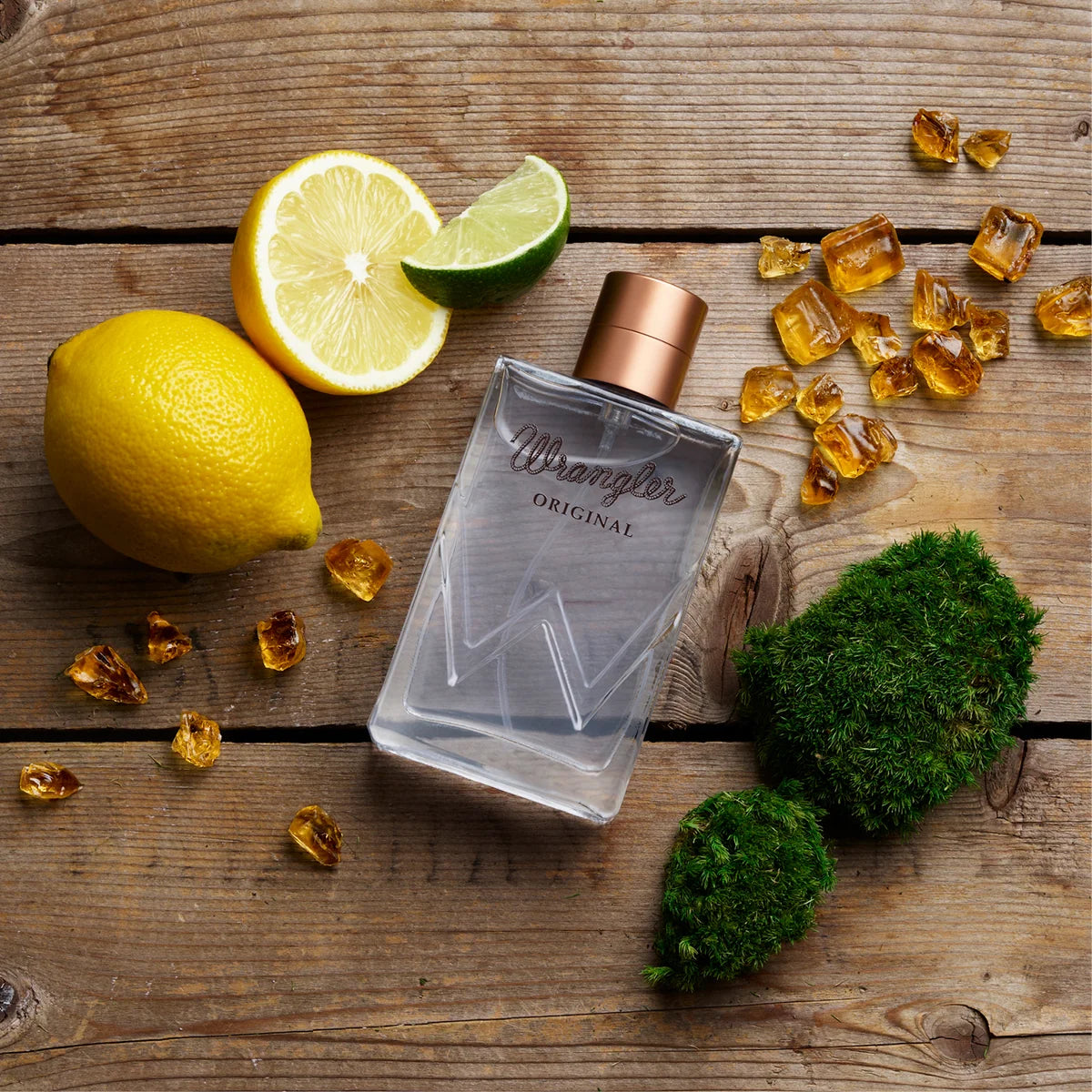 Perfume bottle labeled 'Wrangler Original' on a wooden surface with lemons, lime, and amber gummy bears.