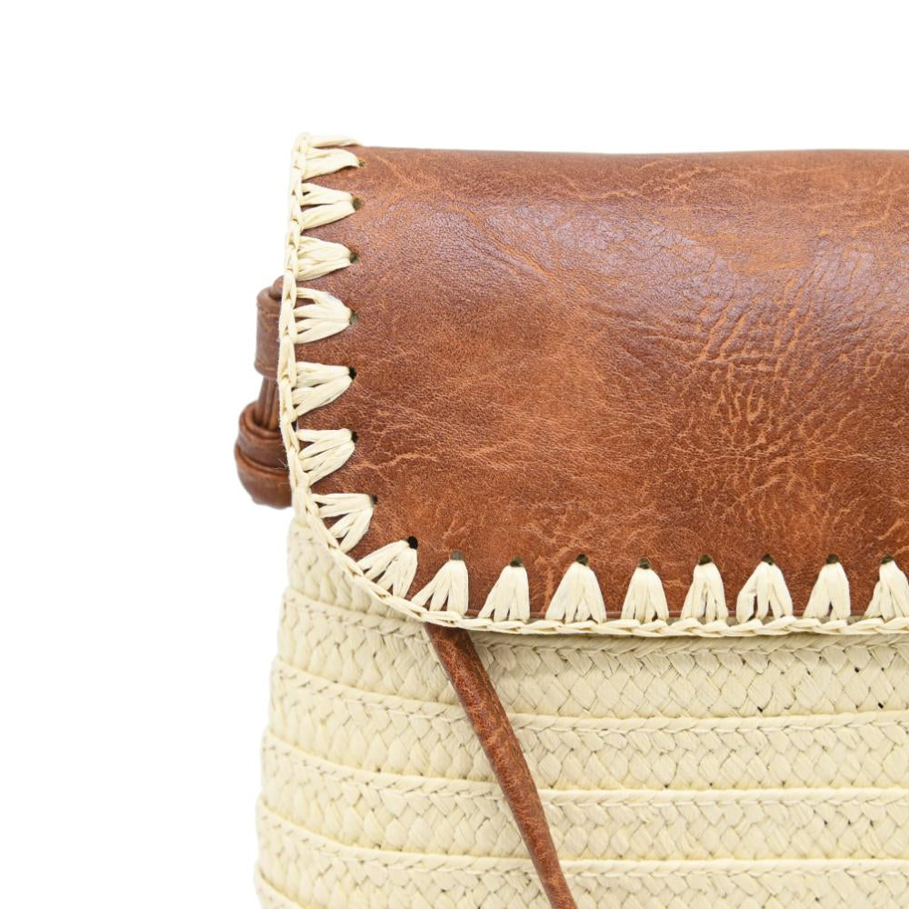 Close-up of a woven straw bag with a brown leather flap and cream braided trim along the edge, on a white background.
