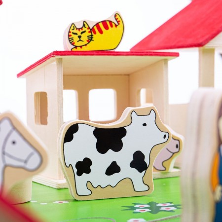 Bigjigs Toys Play Farm. Wooden toy cow with a red roofed house and other animal toys in the background