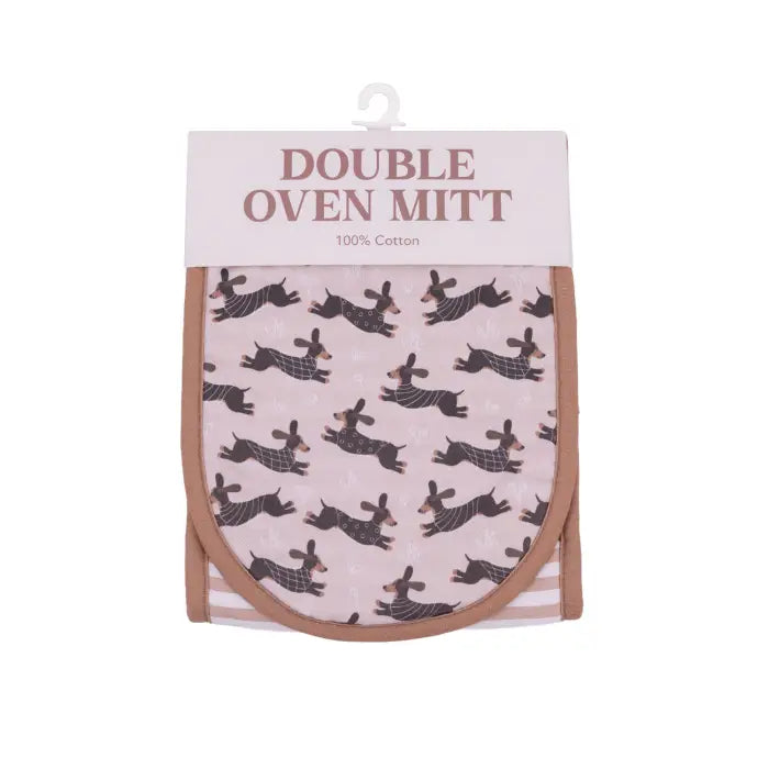 A double oven mitt in pink with a black dachshund pattern, packaged in a white cardboard sleeve with a hanger.