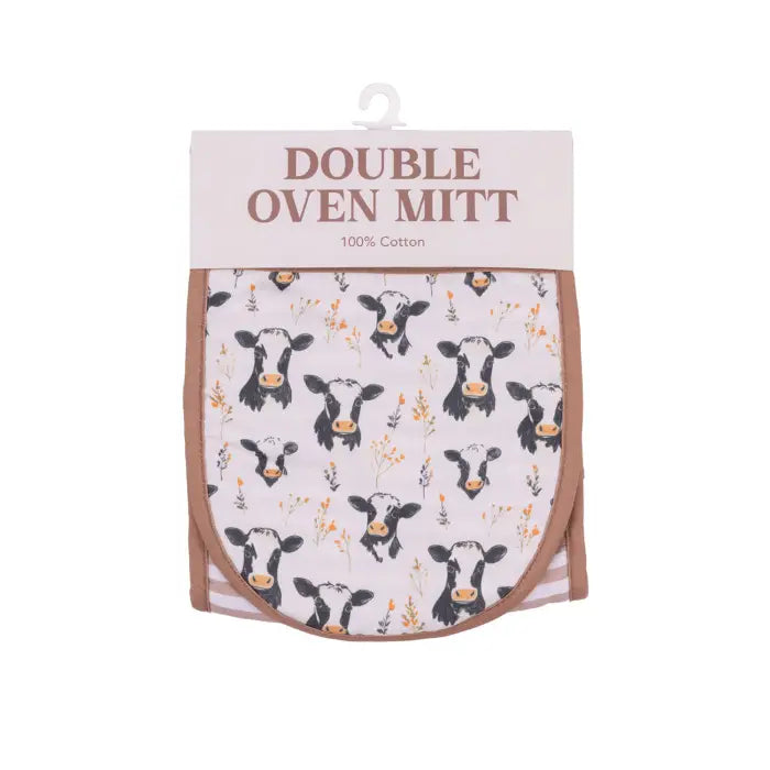 A double oven mitt in its retail packaging, featuring a cow pattern on a light pink background with a brown border and a white header card.