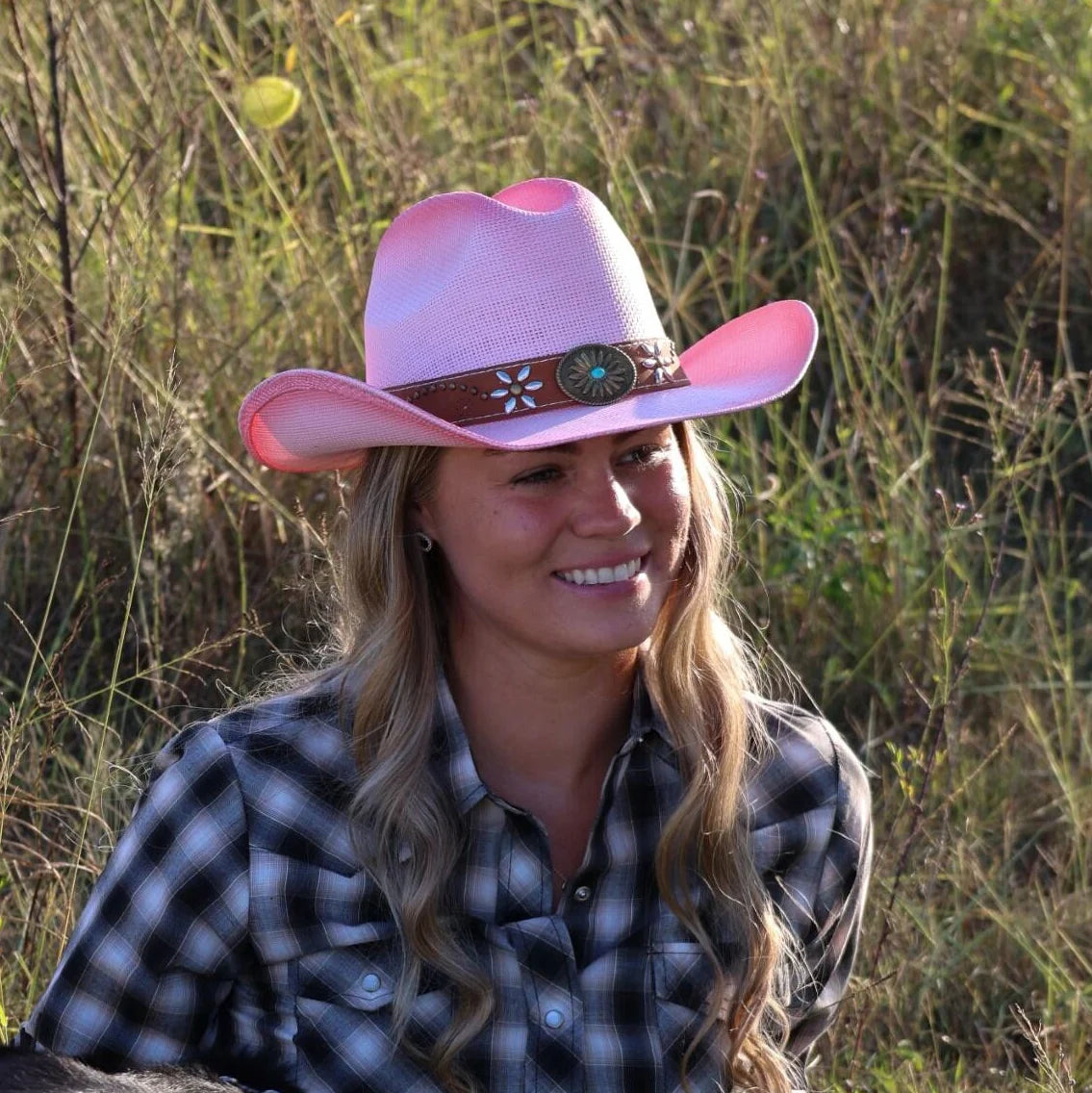 Woman wearing a pink cowboy hat and plaid shirt in a grassy field