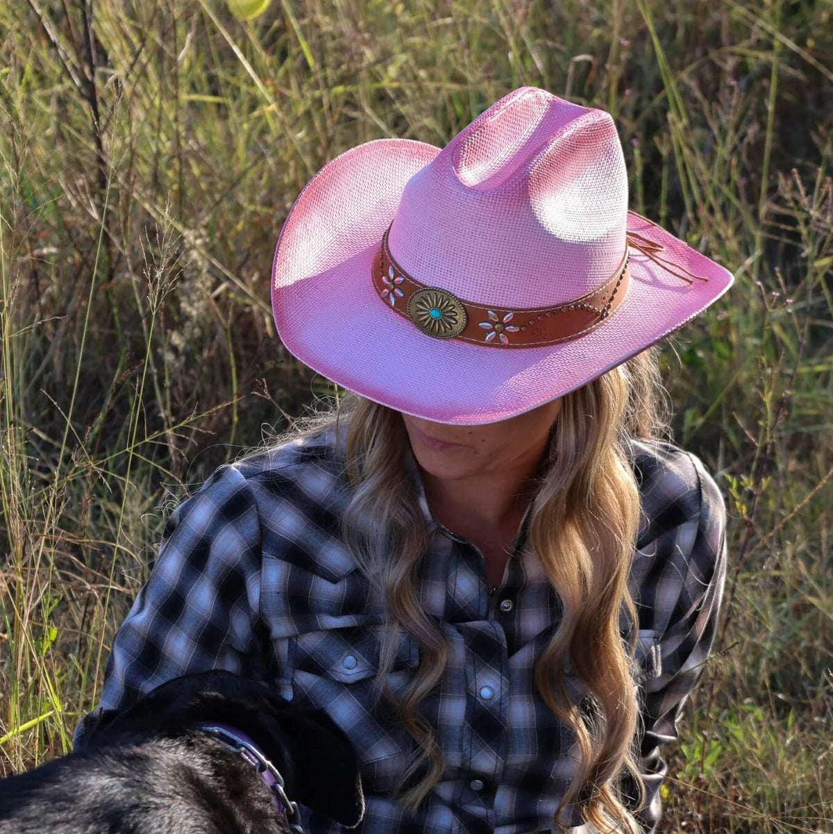 Person wearing a pink cowboy hat and plaid shirt in a grassy field