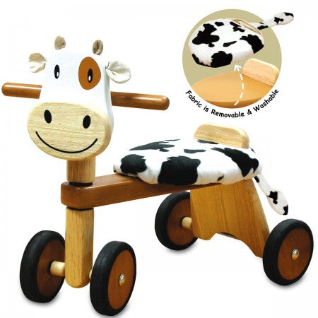 I'm Toy Paddie Rider Calfie. Wooden toy cow with wheels and a detachable cow print seat on a white background