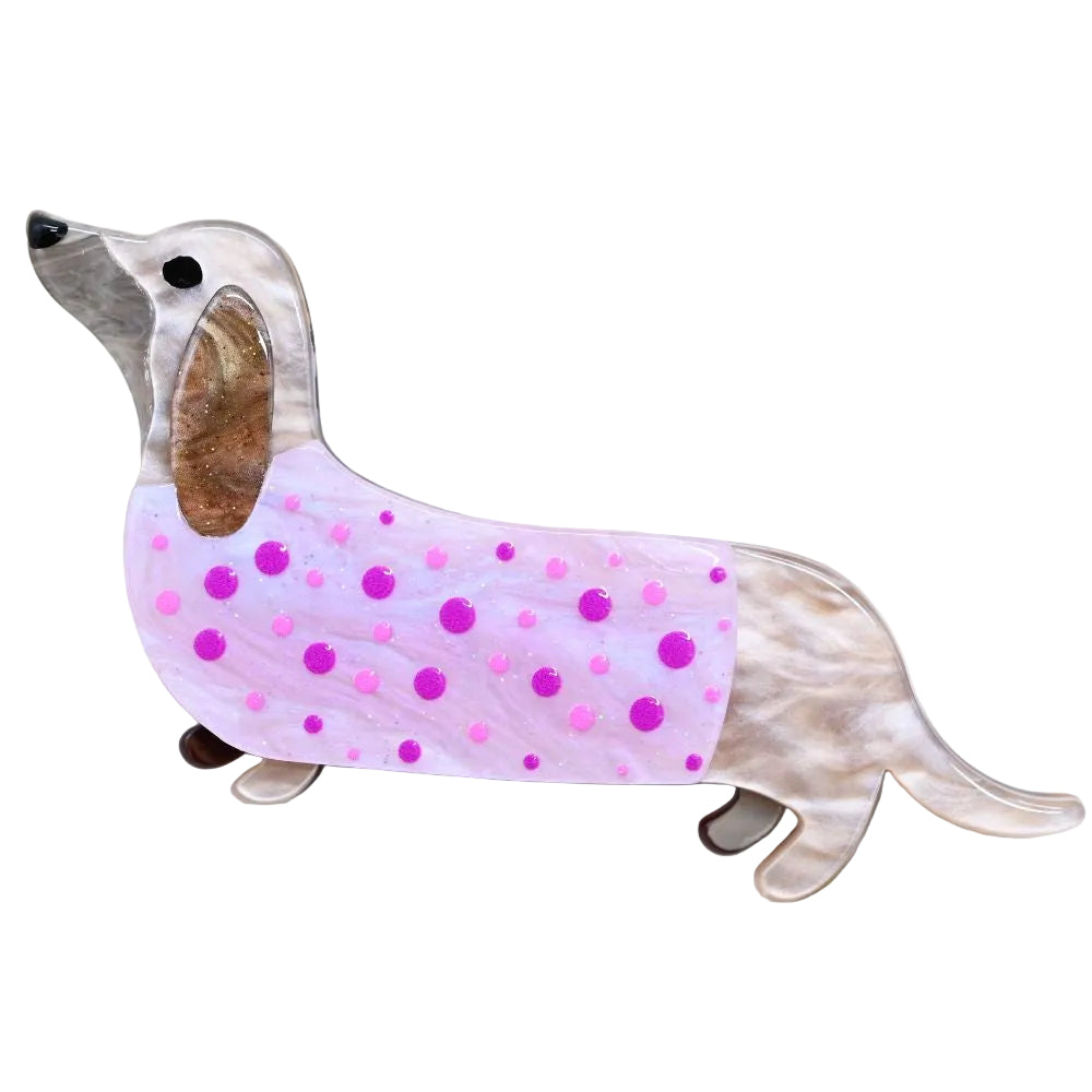 A dachshund-shaped brooch with a pink and lavender marbled body, pink polka dots, and a silver-toned head and legs, resting on a white surface.