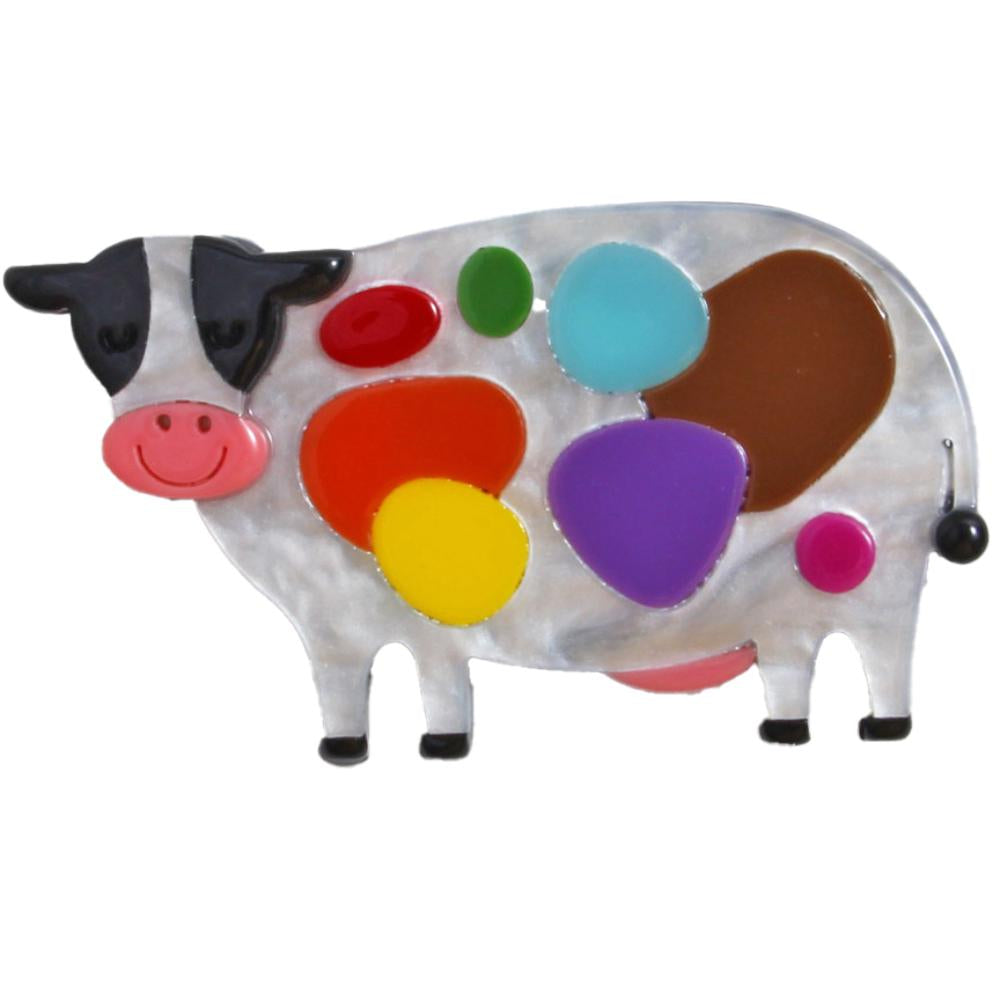 A cow-shaped brooch with a white mother-of-pearl body, black and pink facial features, and colorful enamel spots in red, orange, yellow, green, blue, purple, brown, and pink on a white background.