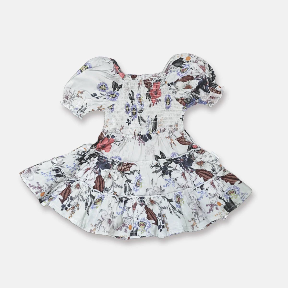 A baby girl's smocked dress with puff sleeves and a ruffled hem, featuring a white base with a colorful floral and butterfly pattern, shown on a light gray background.