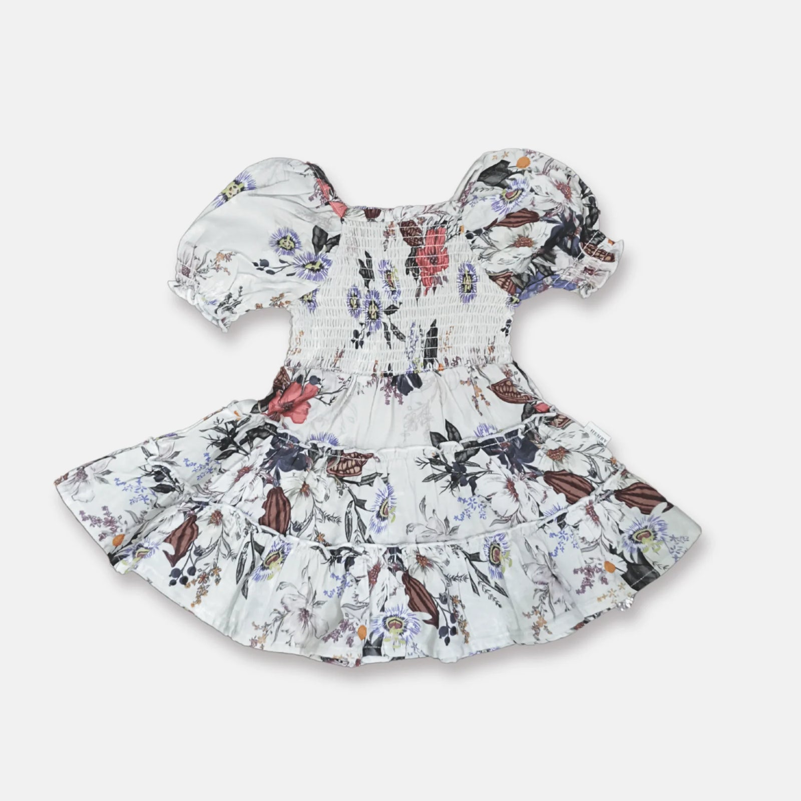 A baby girl's smocked dress with puff sleeves and a ruffled hem, featuring a white base with a colorful floral and butterfly pattern, shown on a light gray background.